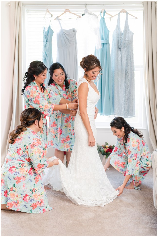 bridesmaids in floral robes help bride get ready with vera wang gowns in background