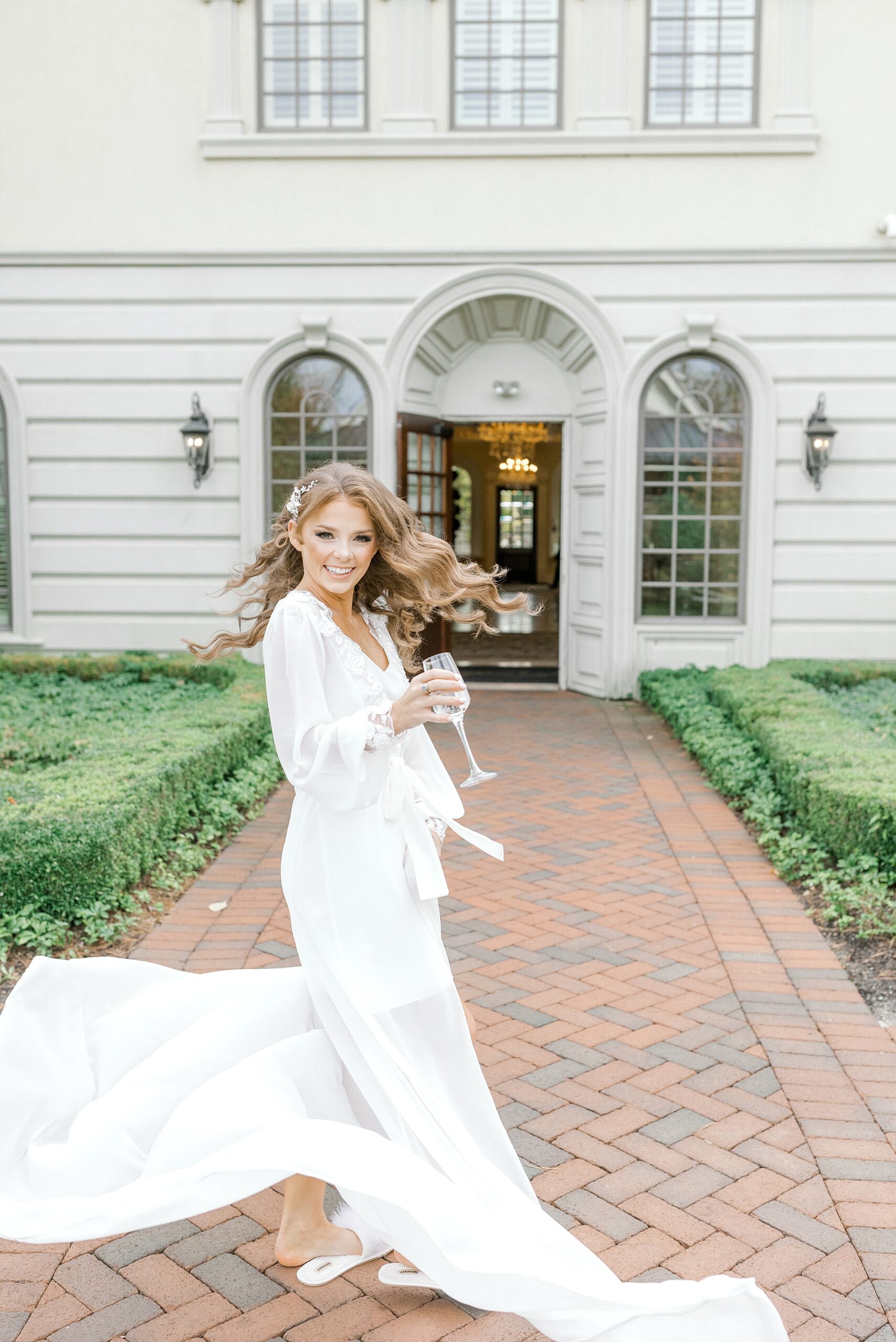 bride twirls in long ivory robe outside Ashford Estate with a glass of champagne