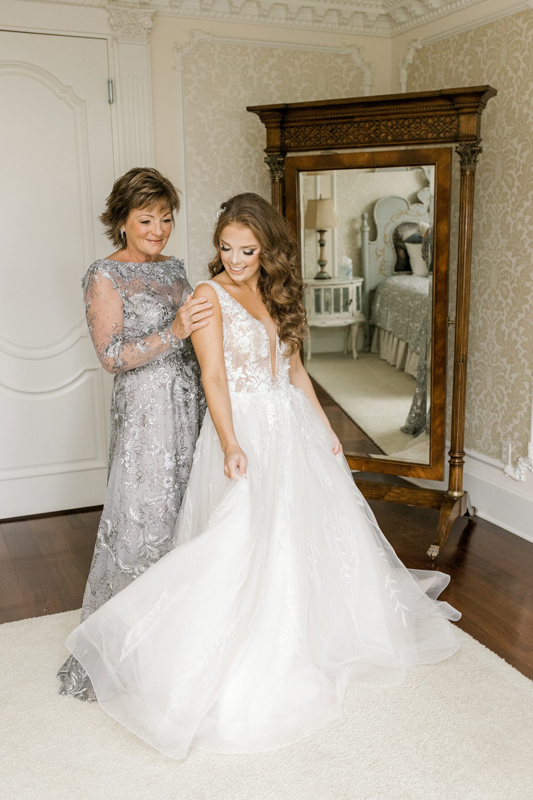 mother in silver dress helps daughter into bridal gown by wooden mirror at the Ashford Estate