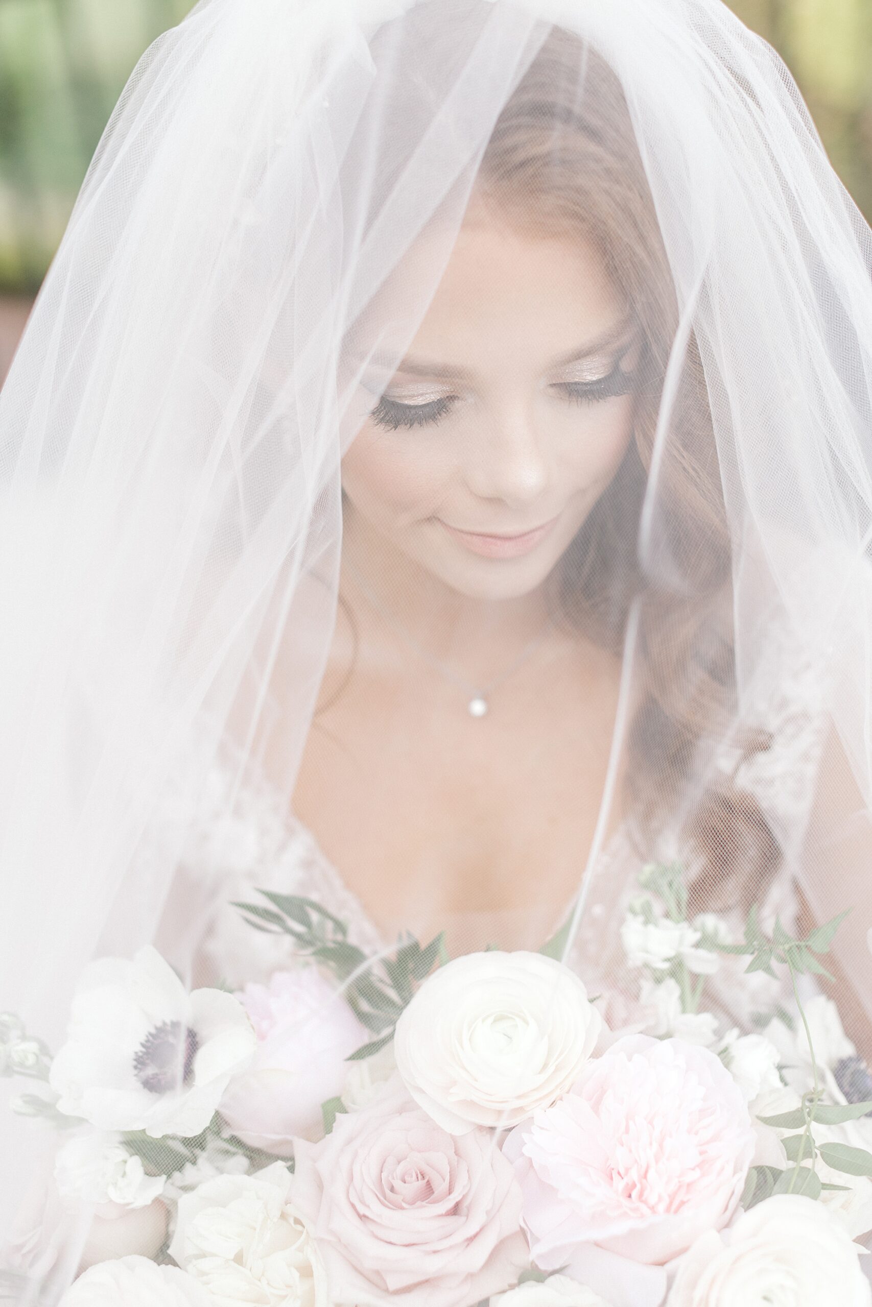 bride looks down at bouquet of pink and white flowers under veil