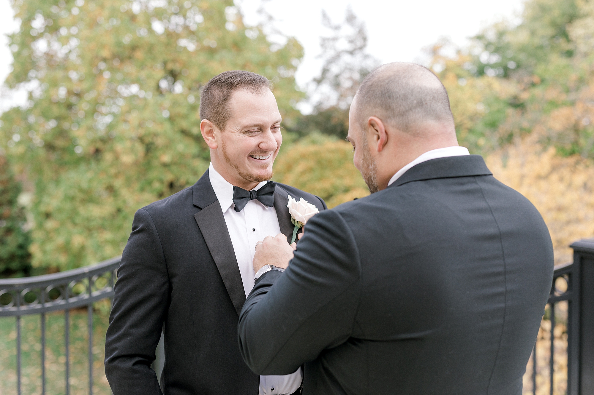 groomsman helps groom with tie of tux