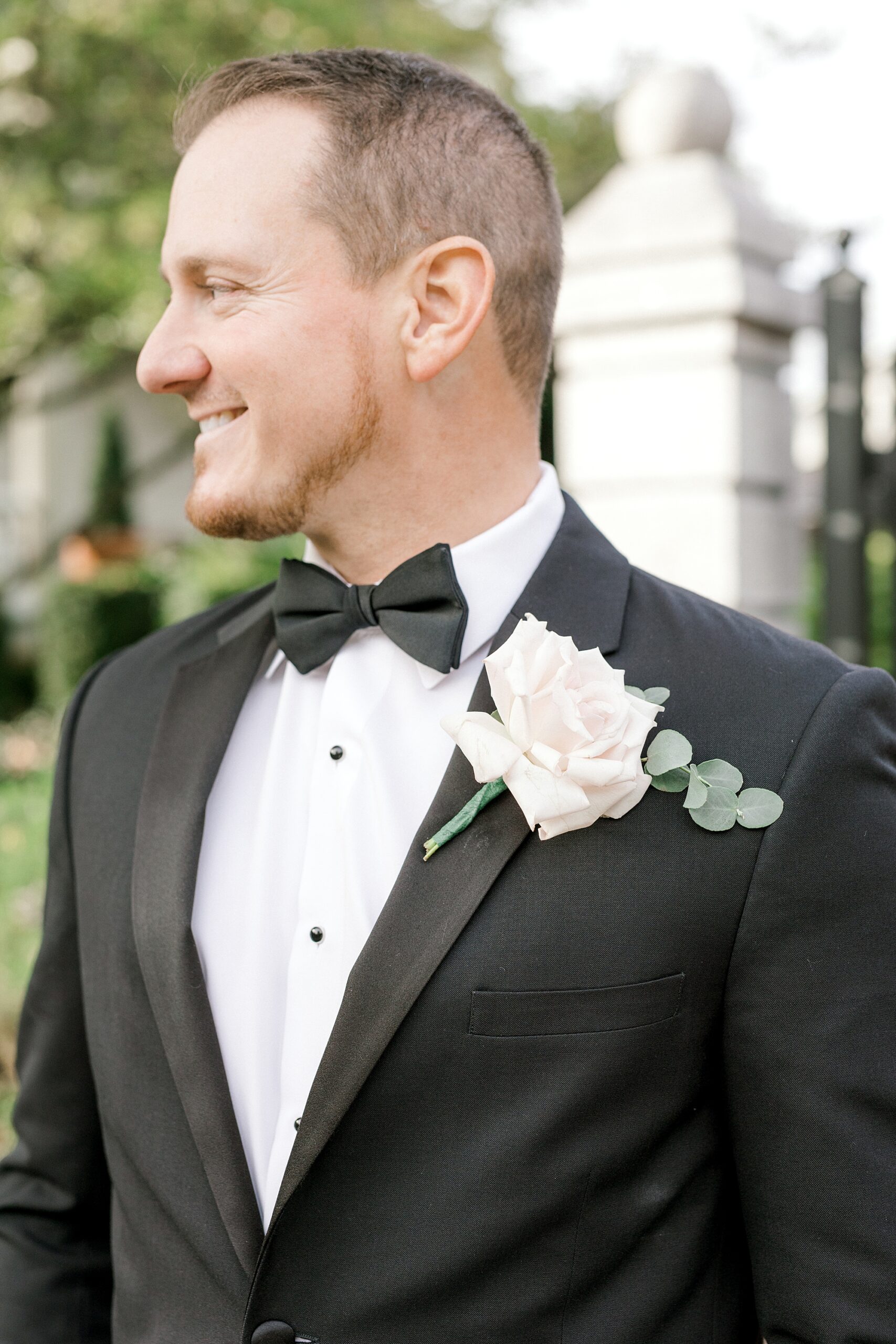 groom smiles over shoulder in black tux jacket with white rose boutonnière