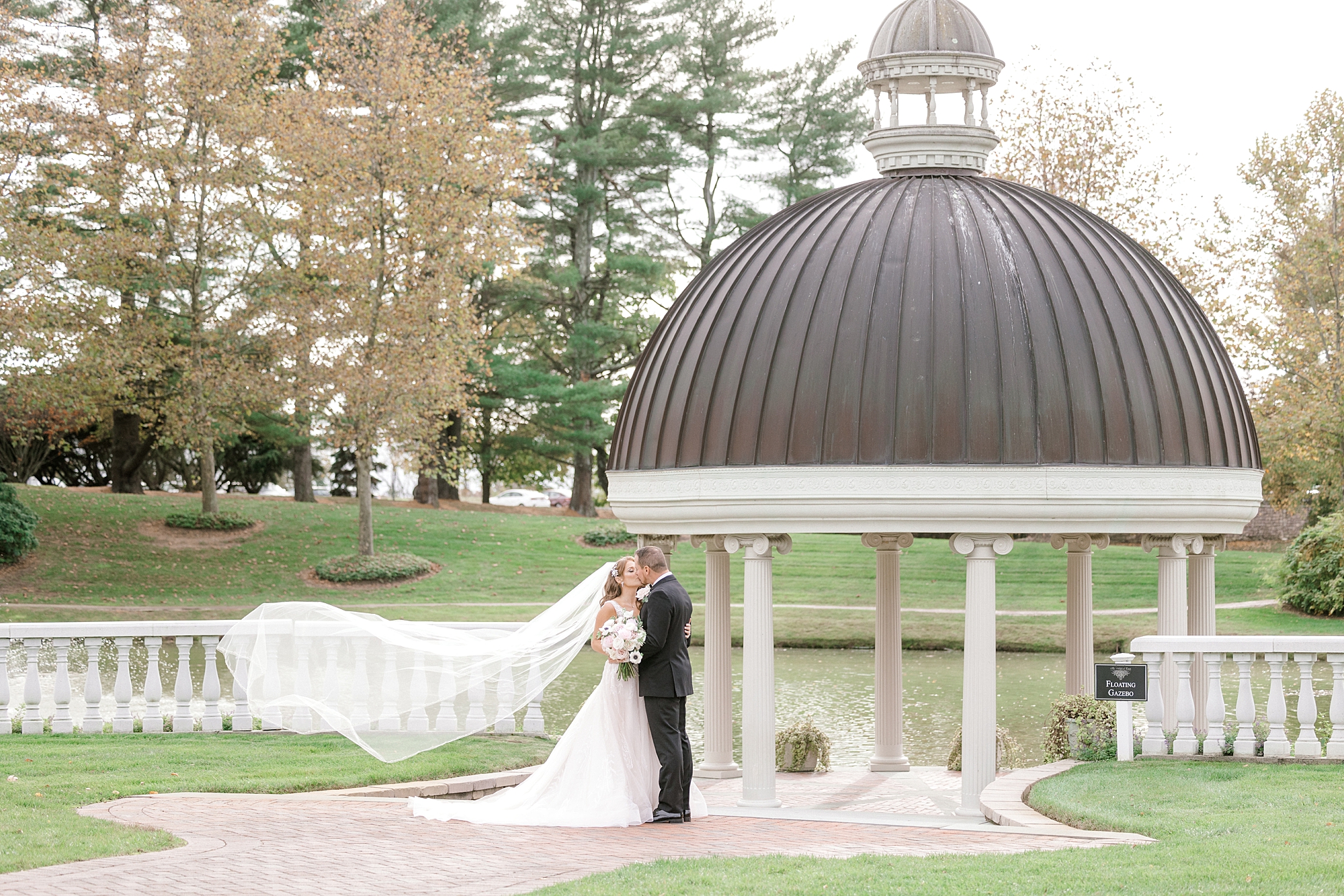 bride and groom kiss near gazebo at the Ashford Estate with bride's veil floating behind them