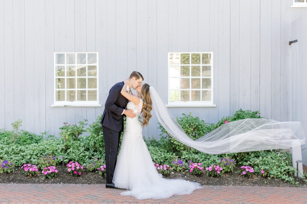 newlyweds kiss outside Bonnet Island Estate with bride's veil floating behind them