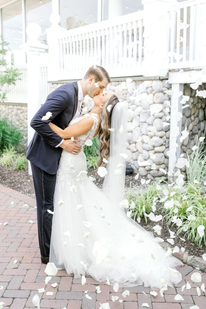 bride and groom kiss with white flower petals falling on them 