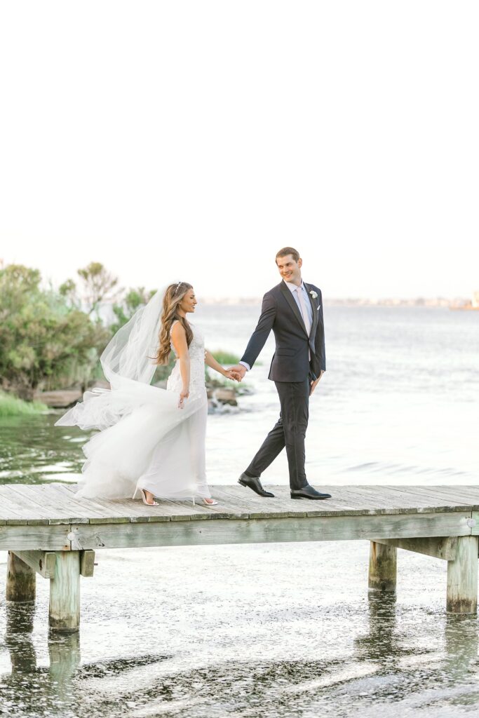 bride and groom hold hands walking on dock outside Bonnet Island Estate
