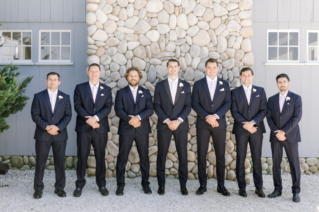 groom stands with groomsmen in navy suits by stone fireplace outside Bonnet Island Estate