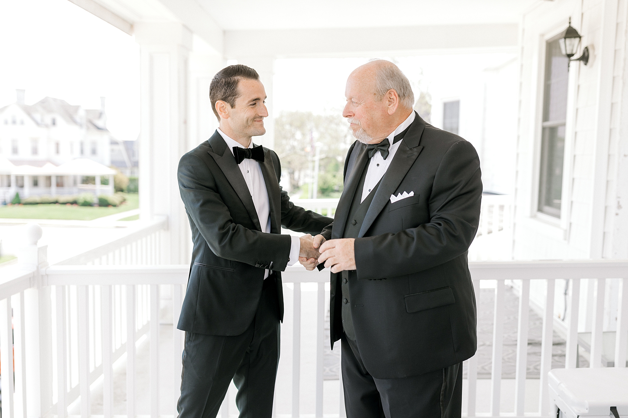 groom in black tux shakes hands with dad on front porch