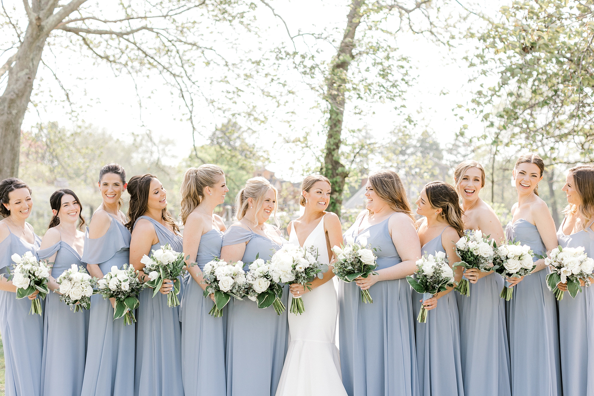 bride smiles with bridesmaids in dusty blue gowns with white bouquets