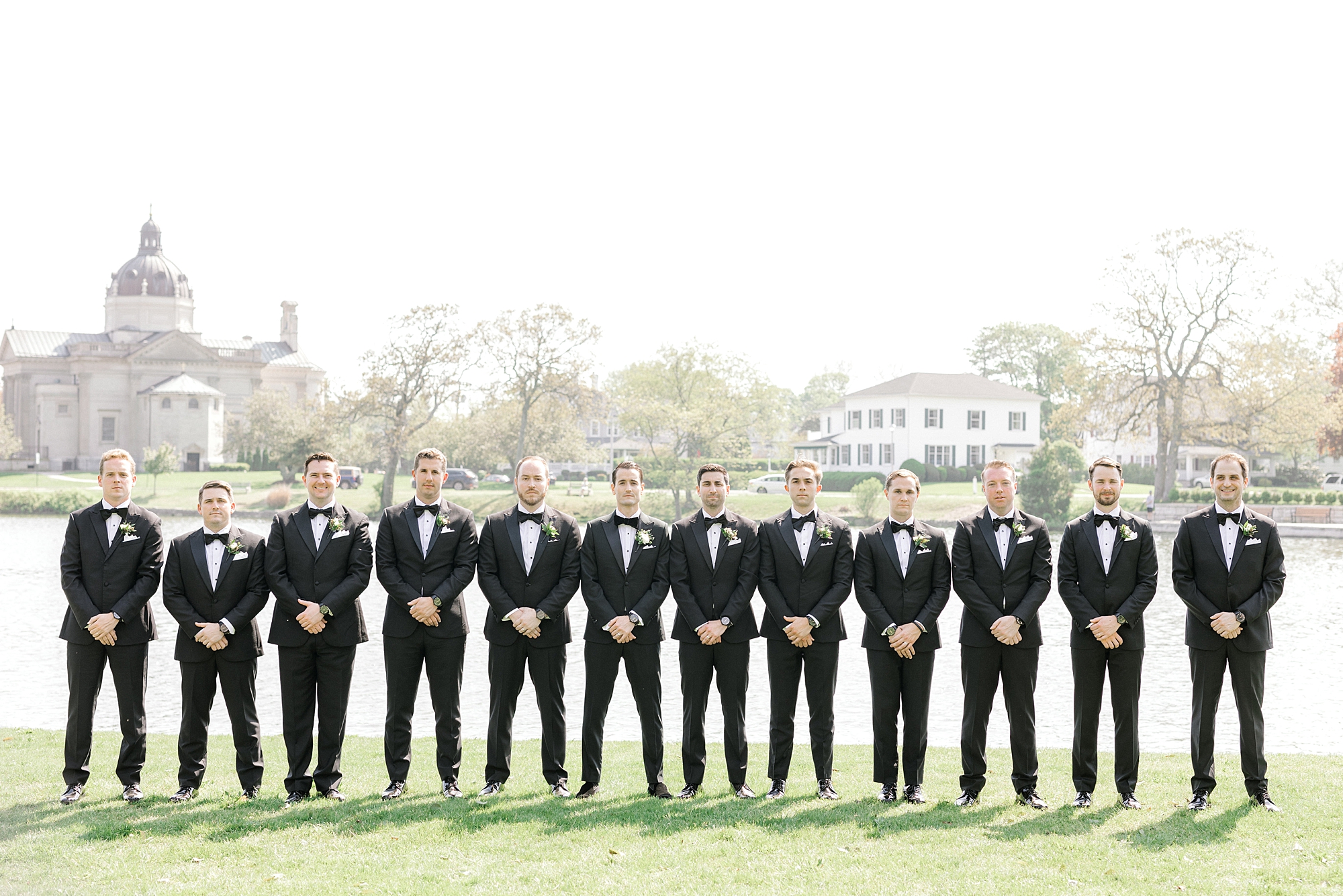 groom poses with groomsmen in black suits along Spring Lake