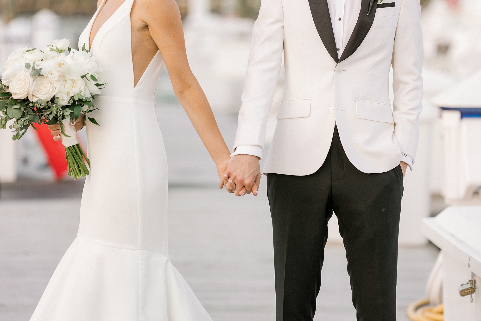 groom in white tux jacket holds hands with bride on dock at Crystal Point Yacht Club