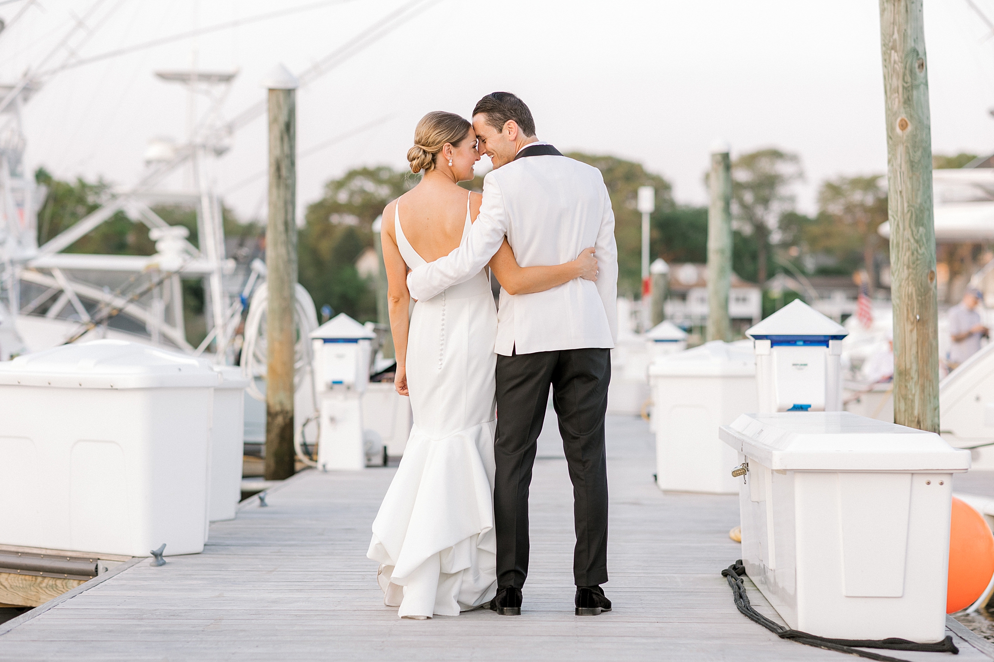 bride and groom walk on dock leaning heads together