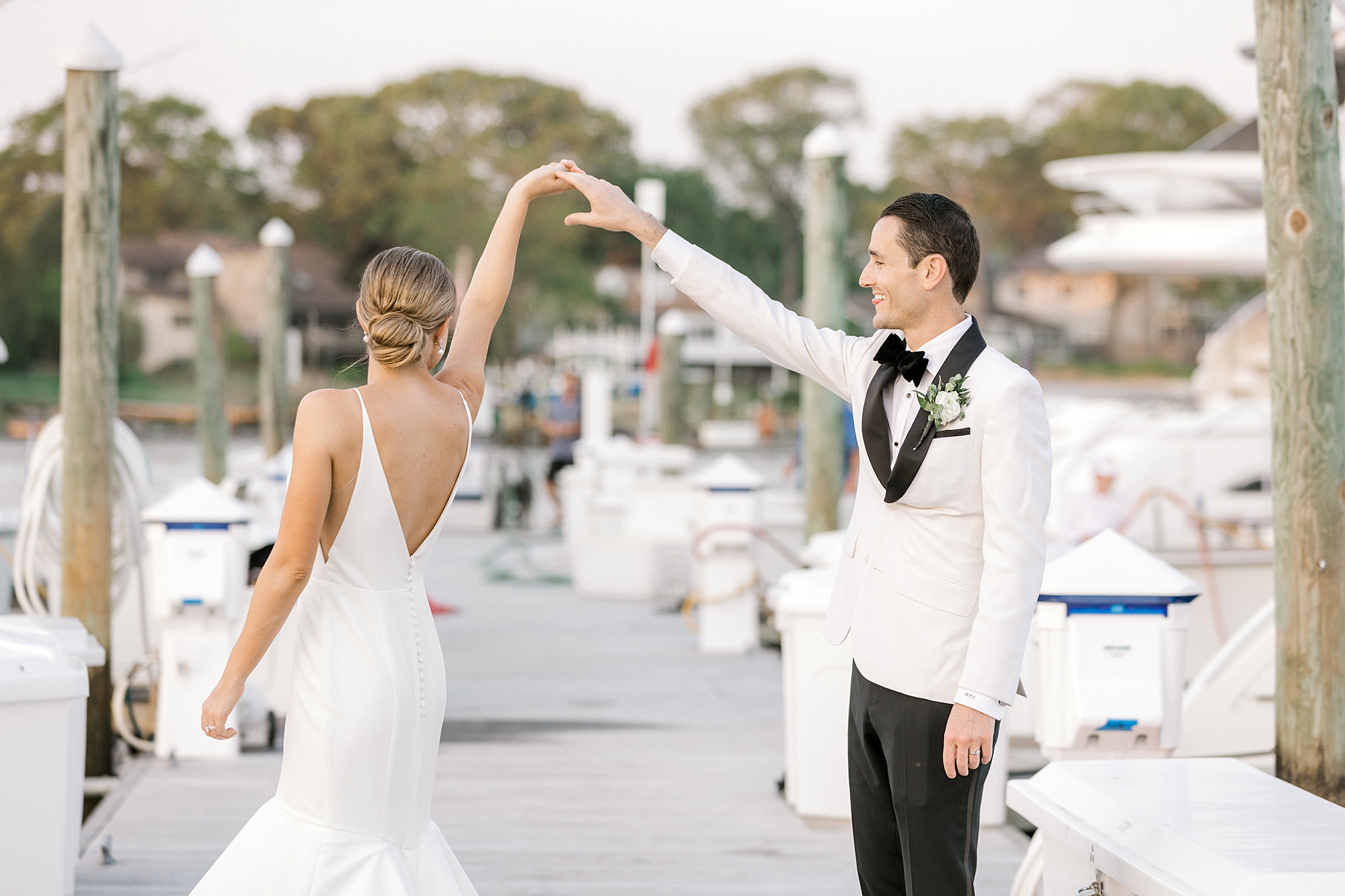 groom in white suit jacket twirls bride on docks at Crystal Point Yacht Club