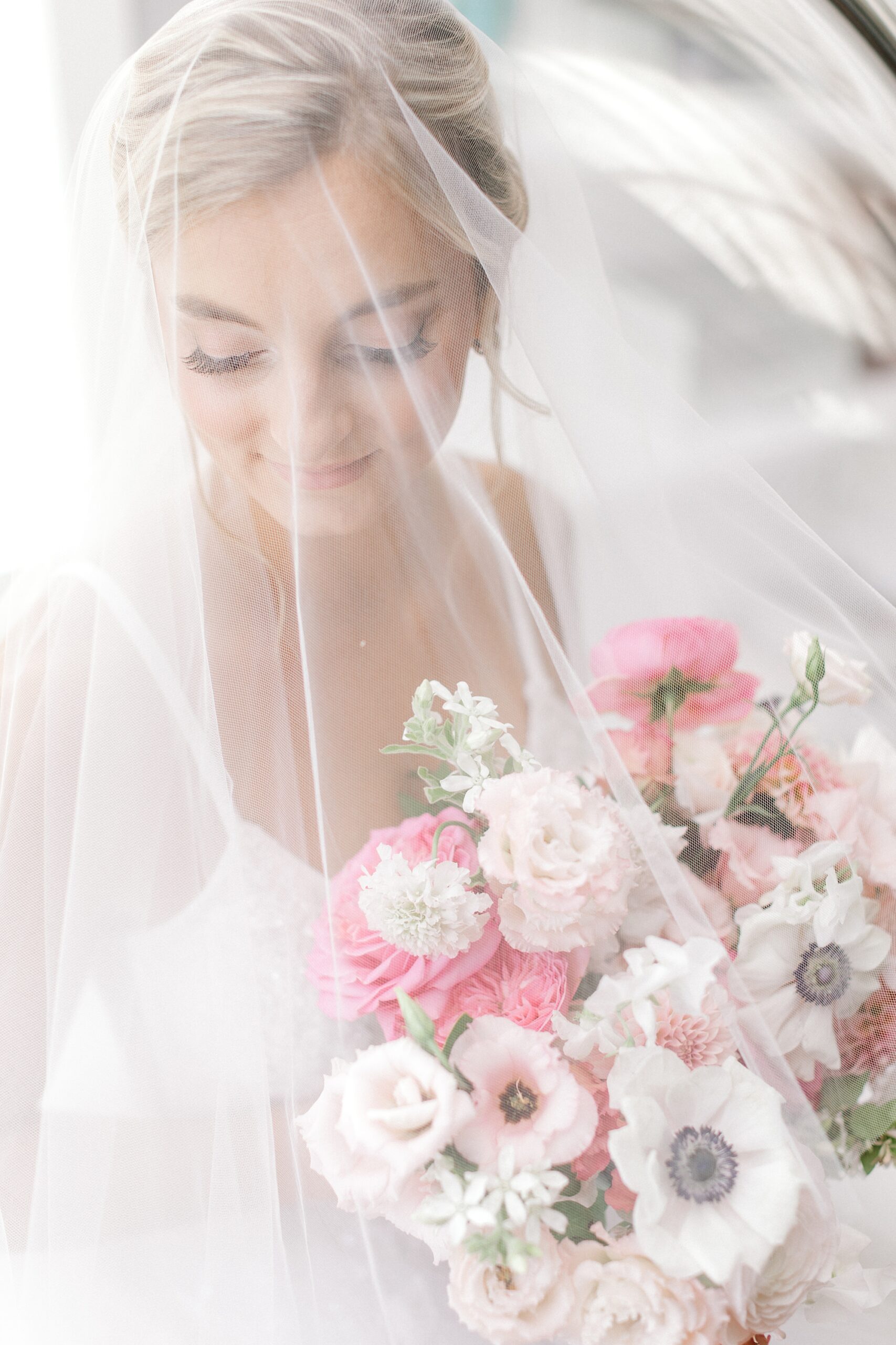 bride sits under veil with bouquet of pink flowers and anemones