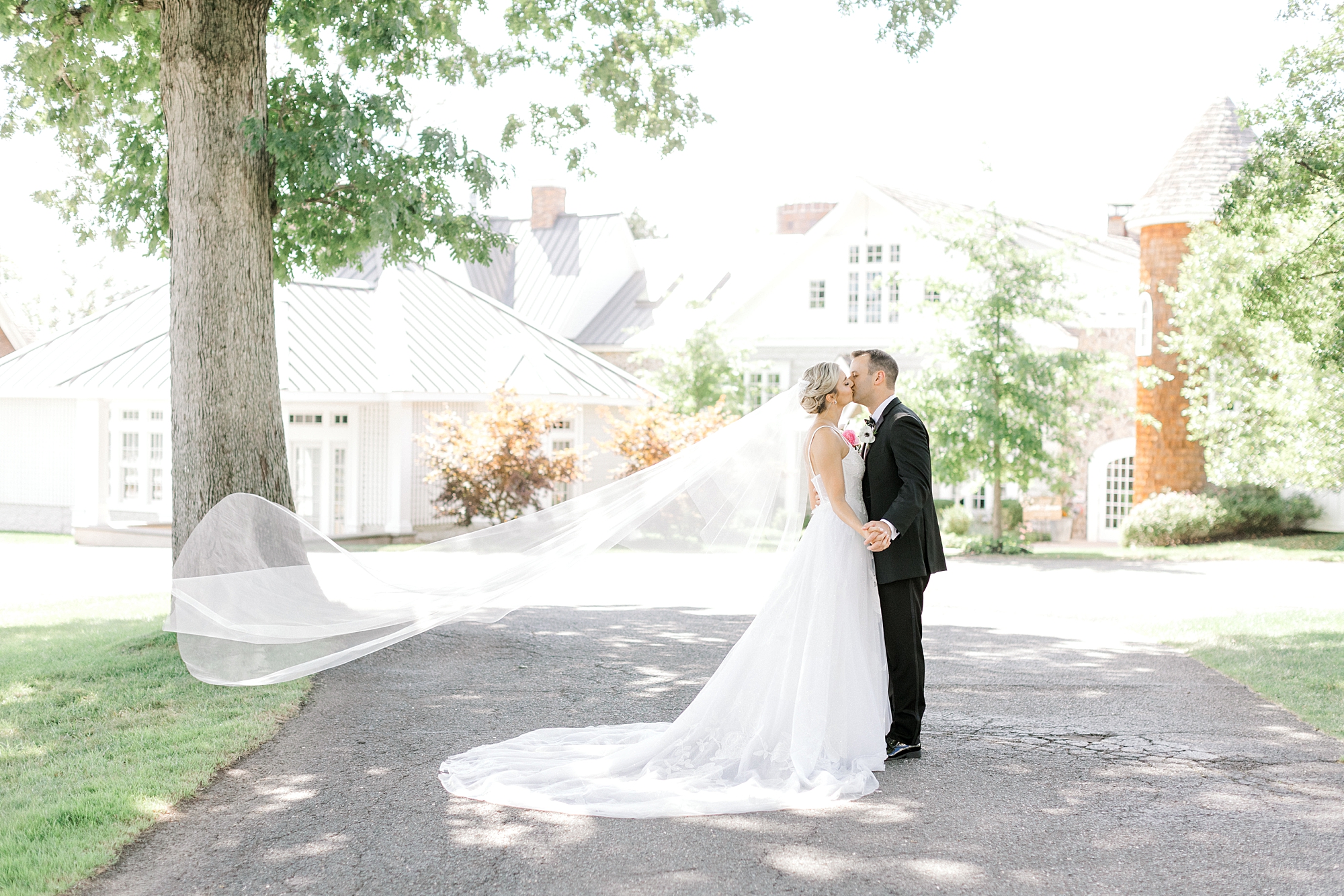 newlyweds kiss in front of Ryland Inn with bride's veil floating behind them