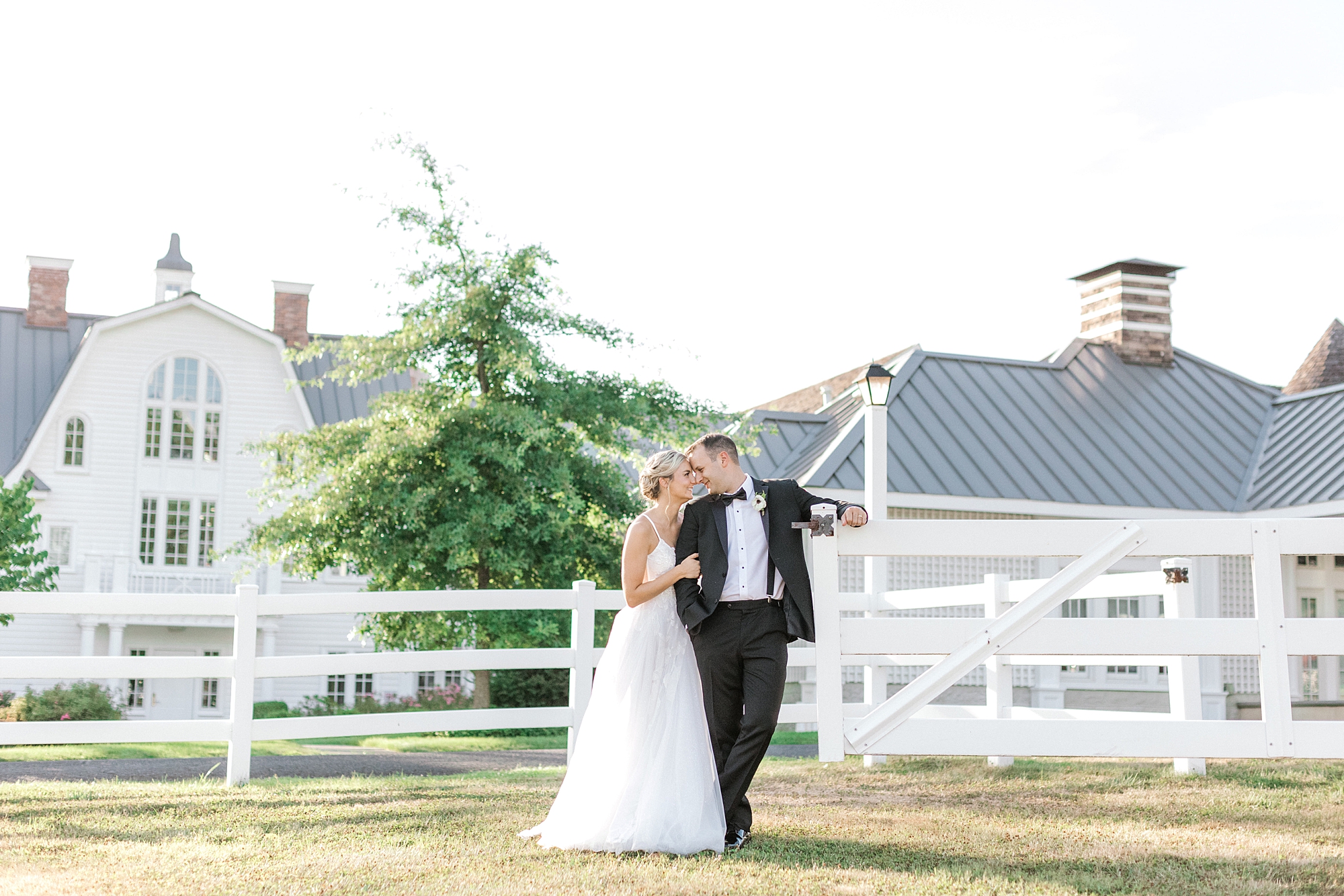 bride and groom lean against white fence outside Ryland Inn