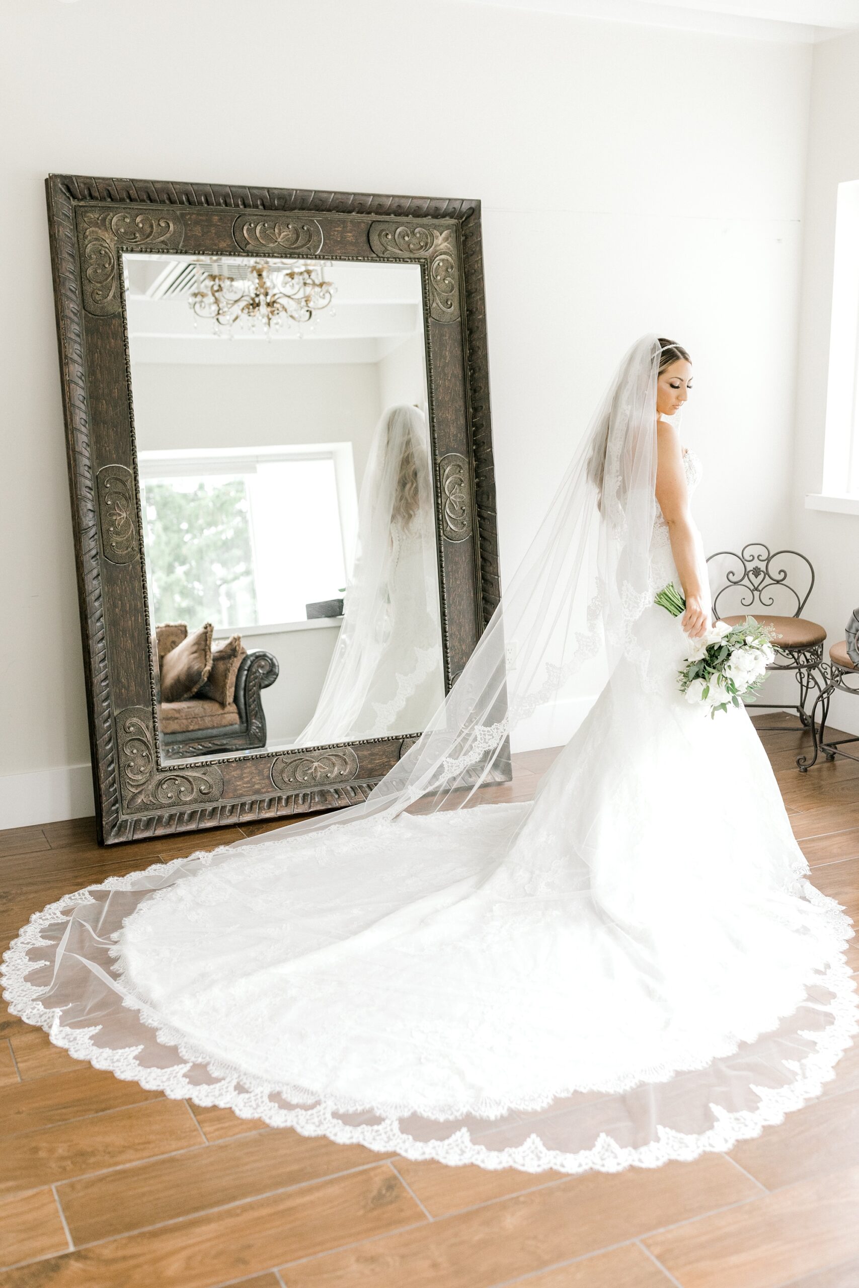 bride poses by mirror with train of dress and veil out