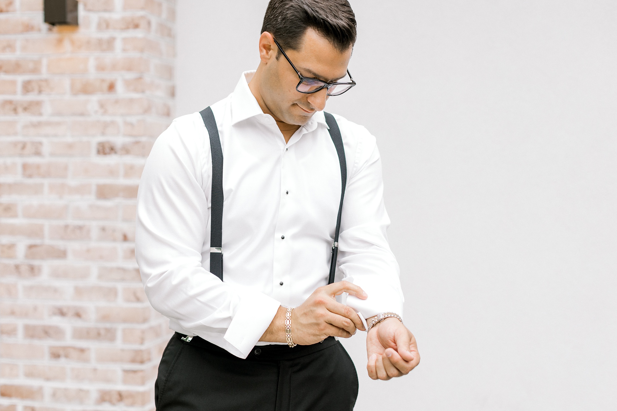 groom stands adjusting cufflinks in suspenders
