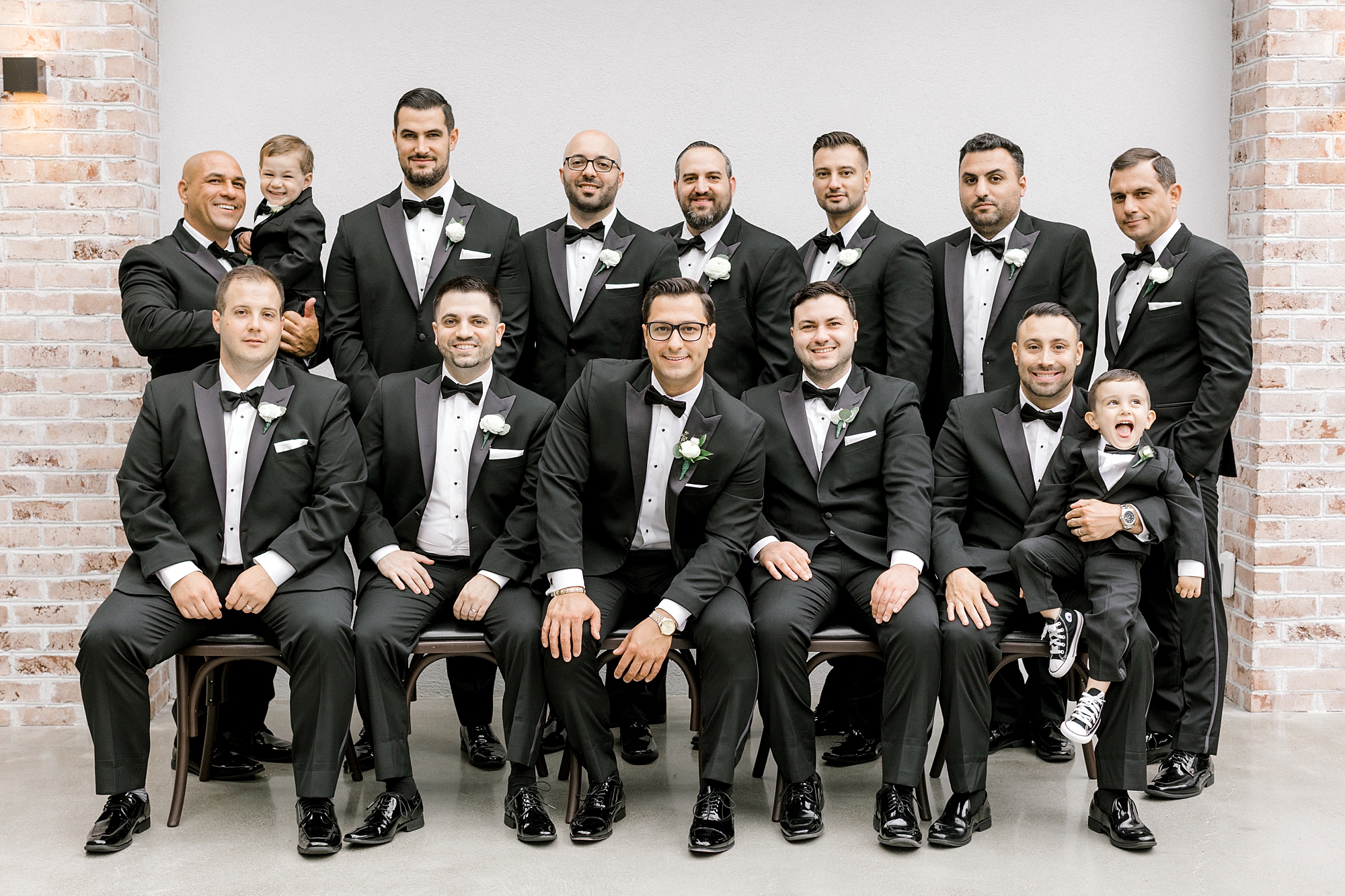 groom sits with groomsmen in black suits between brick walls