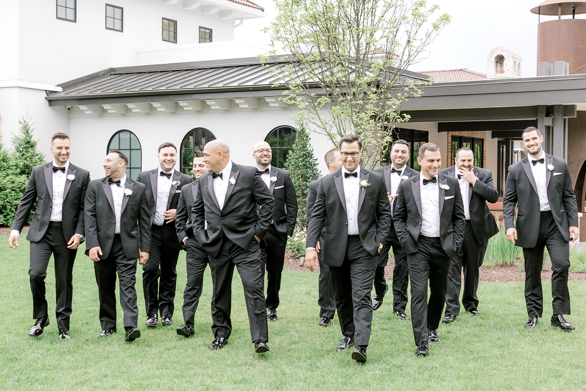 groom walks with groomsmen across lawn at The Refinery at Perona Farms