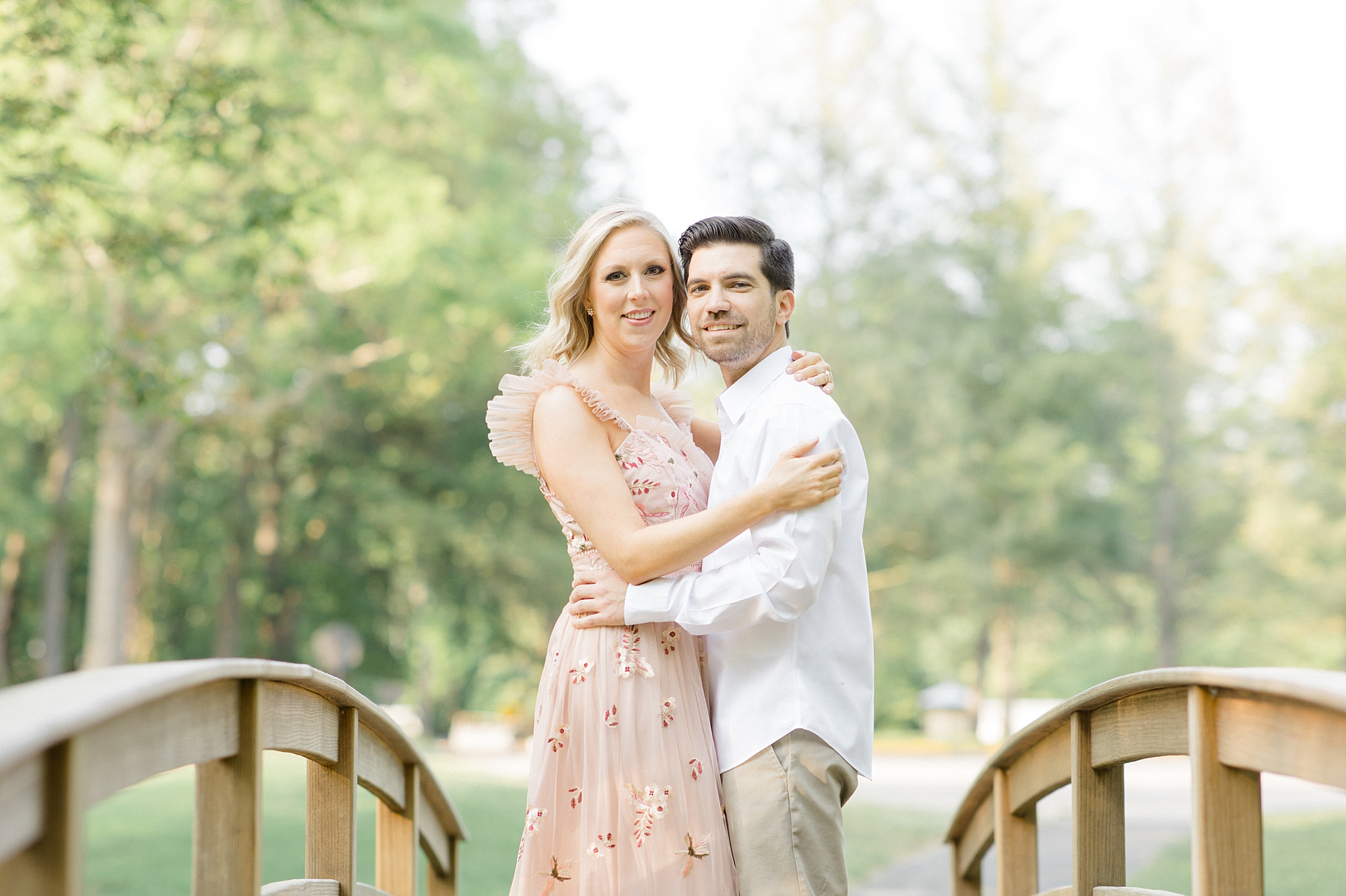 engaged couple hugs cheek to cheek on wooden bridge in Allaire State Park