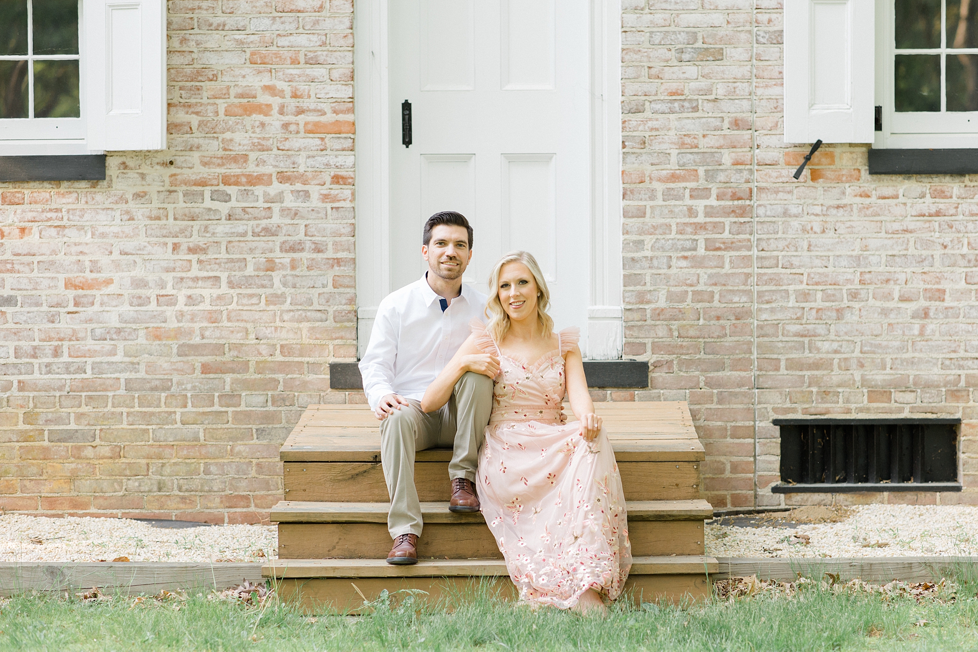 woman leans on man's leg sitting on steps during engagement session in Allaire State Park