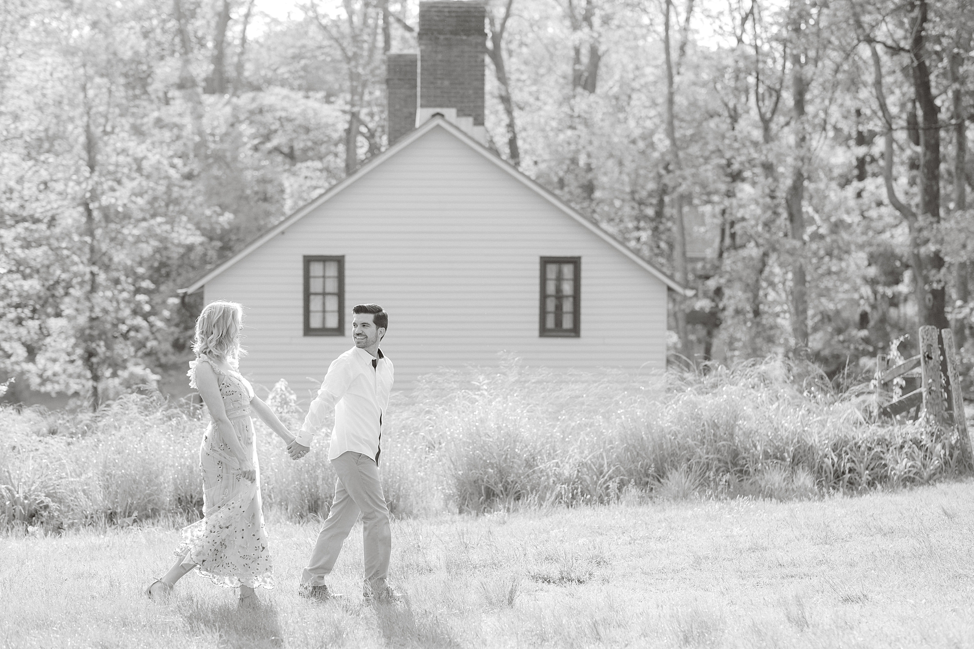 engaged couple holds hands walking through field at Allaire State Park