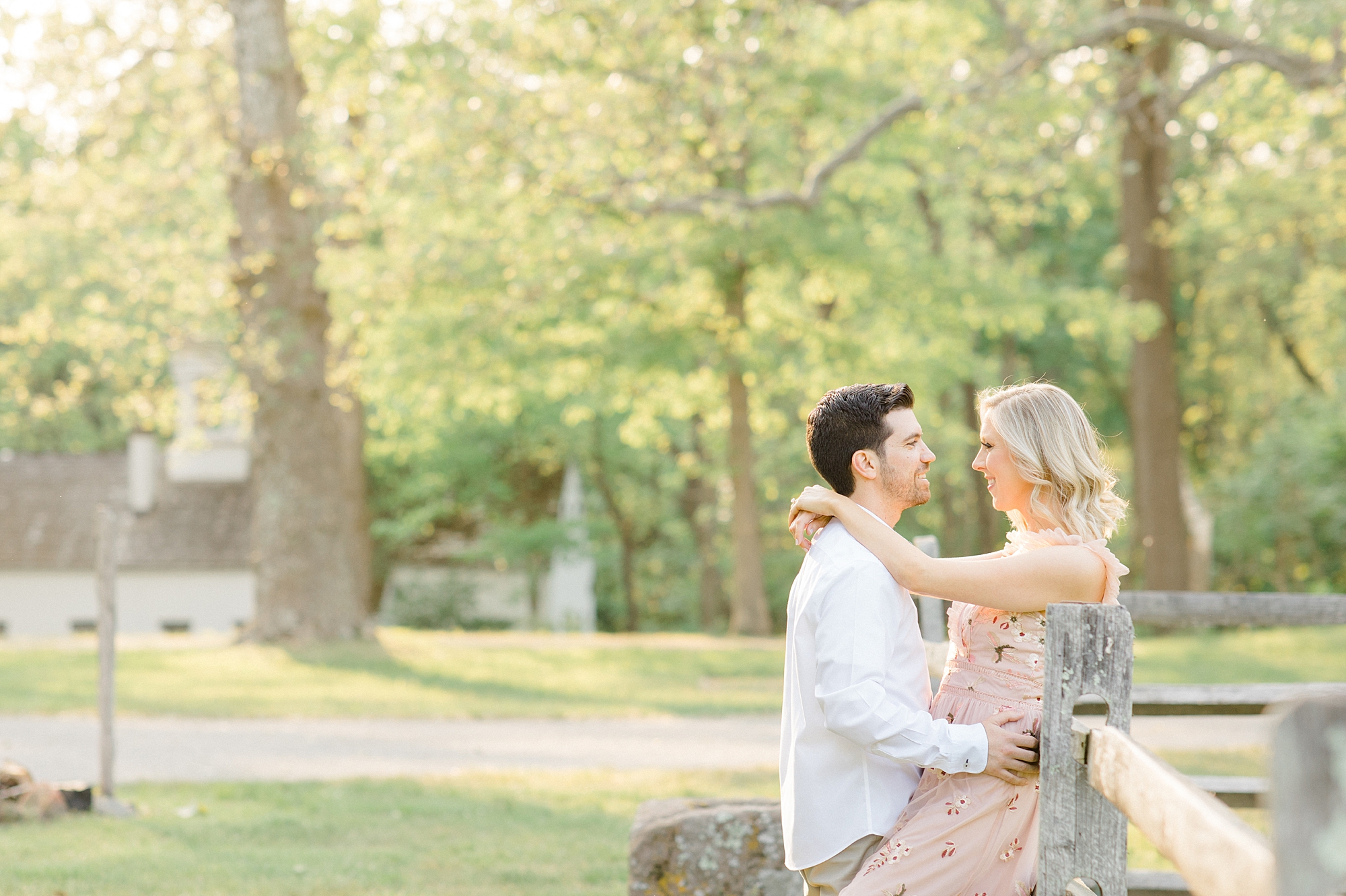 man leans woman against wooden fence during springtime Allaire State Park engagement session