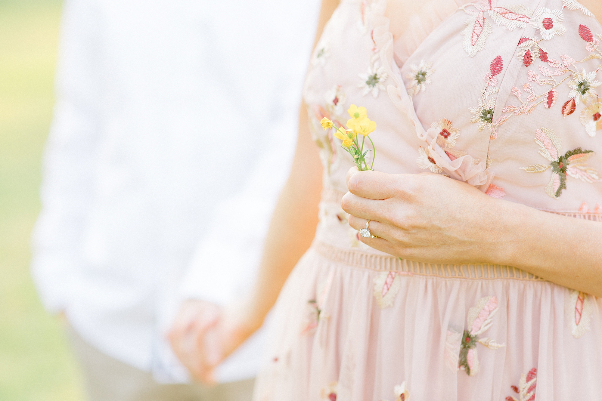 woman in pink floral dress holds hands with man and yellow flowers in other hand