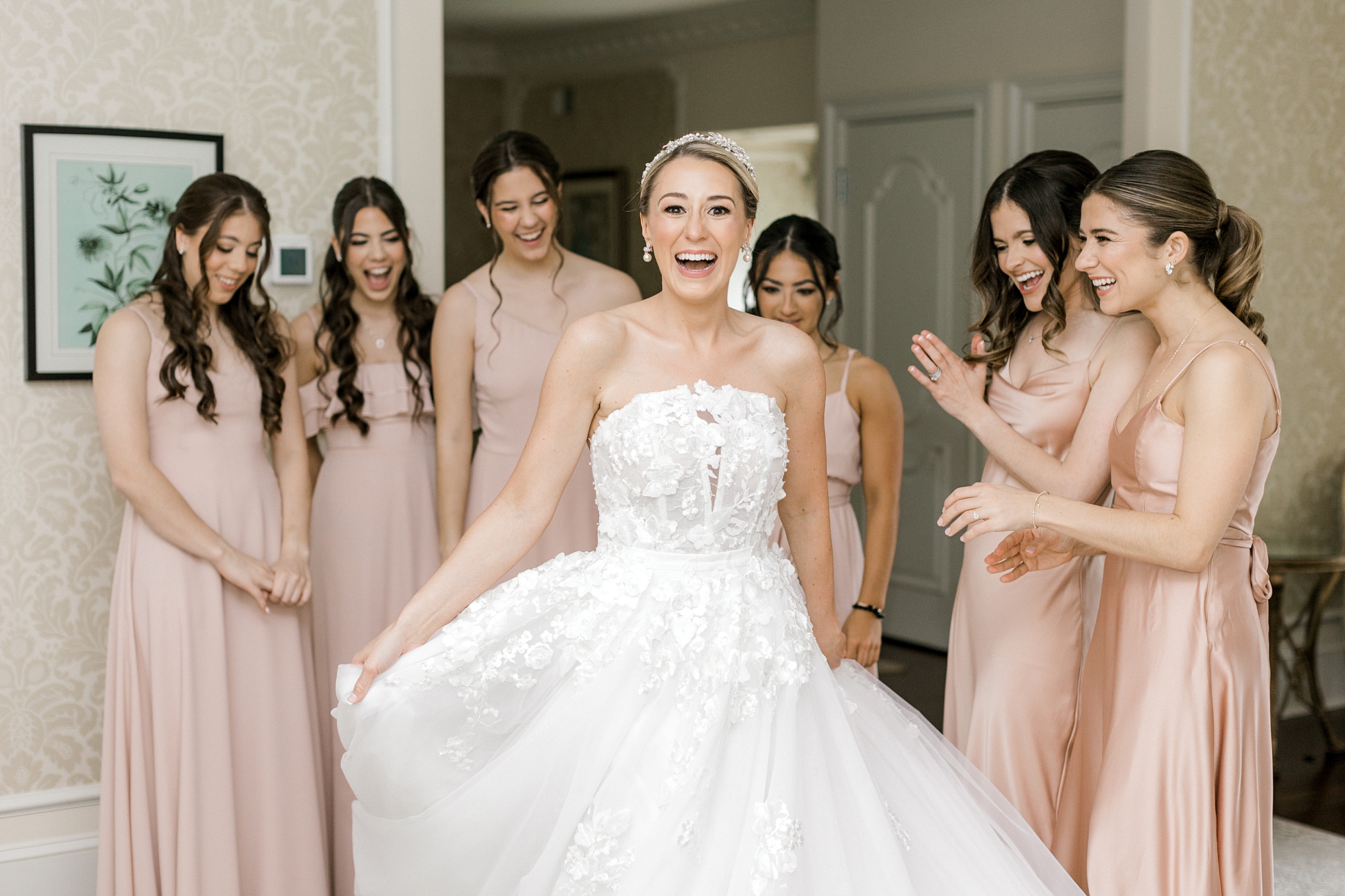 bridesmaids in pink gowns help bride with wedding dress with flower accents