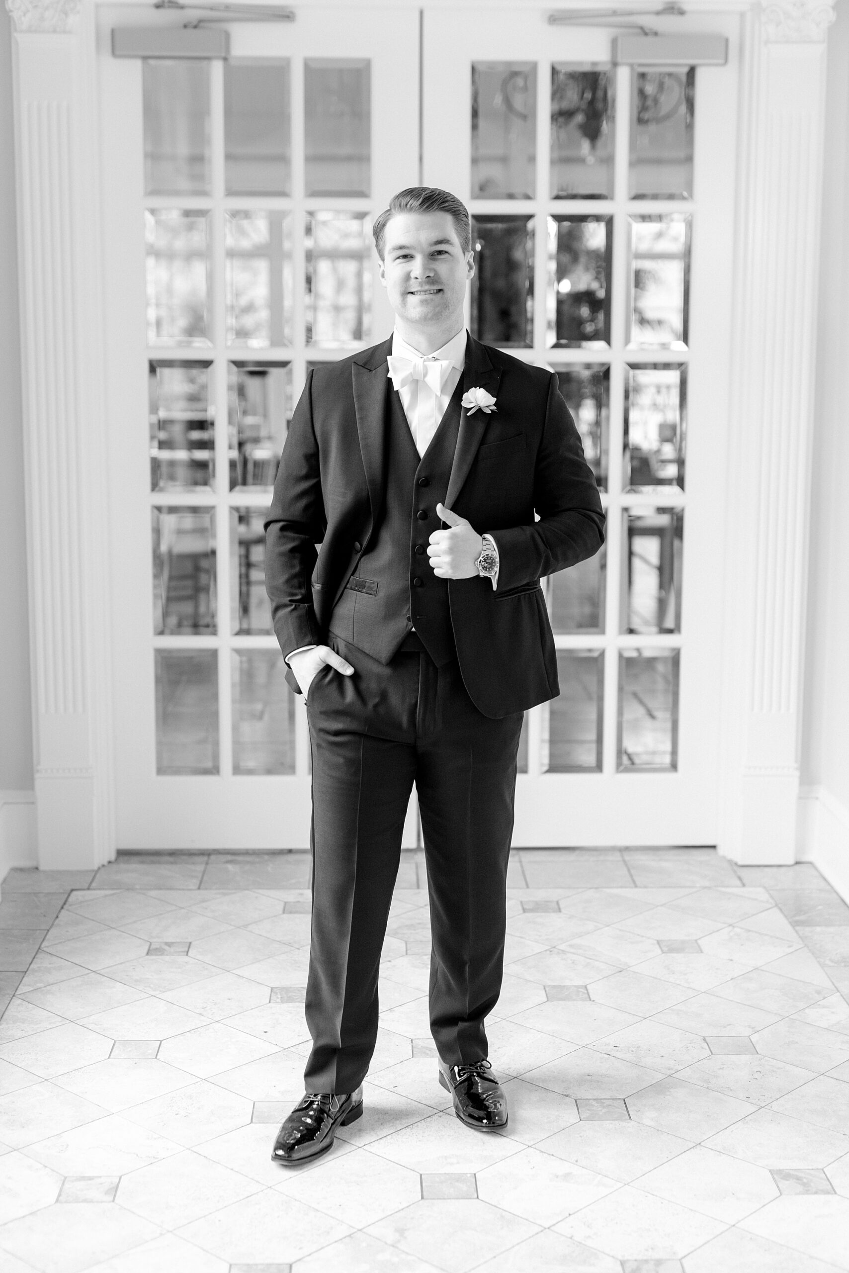 groom stands in lobby holding lapel of suit