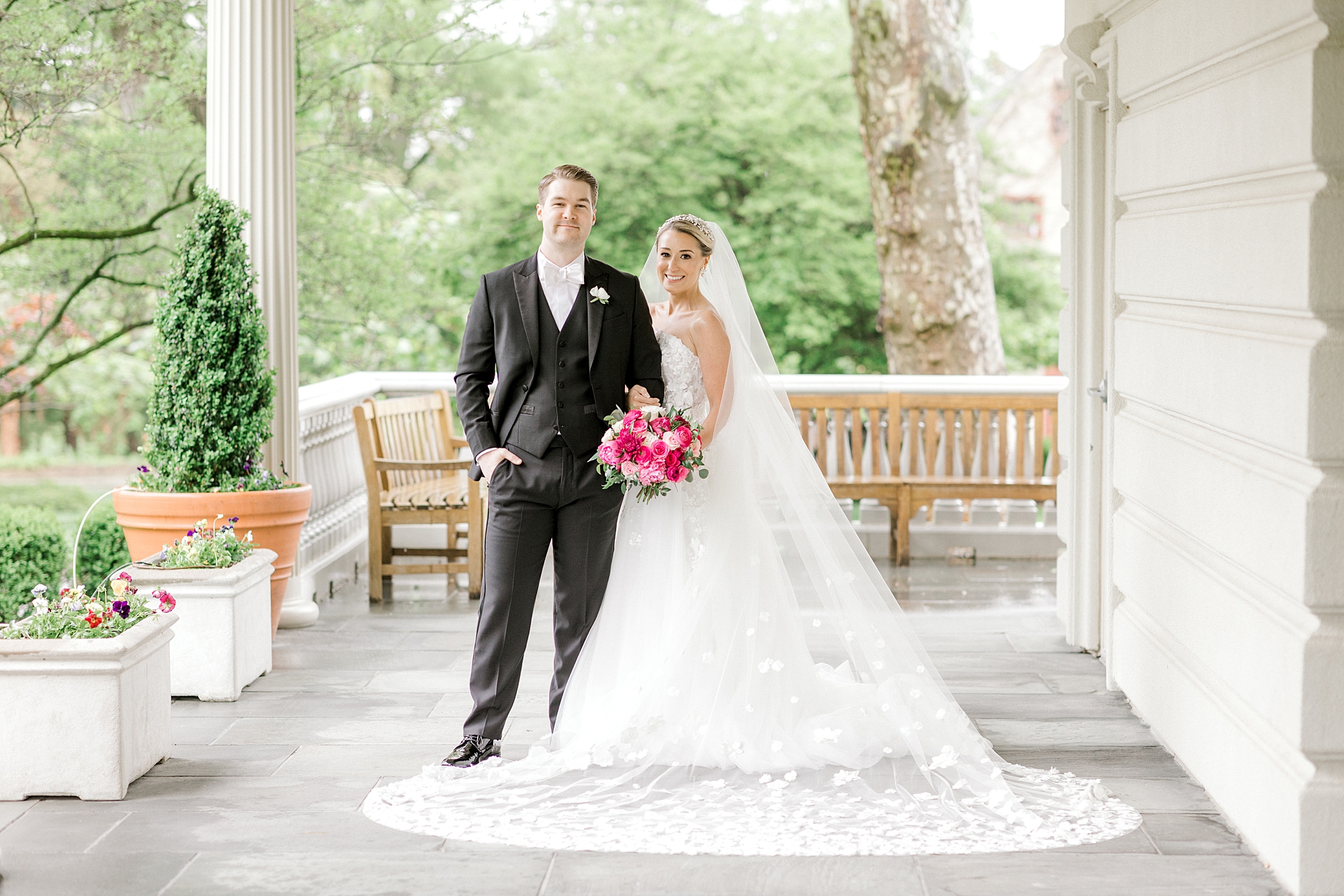 bride holds groom's arm and bouquet of pink flowers on patio at the Ashford Estate