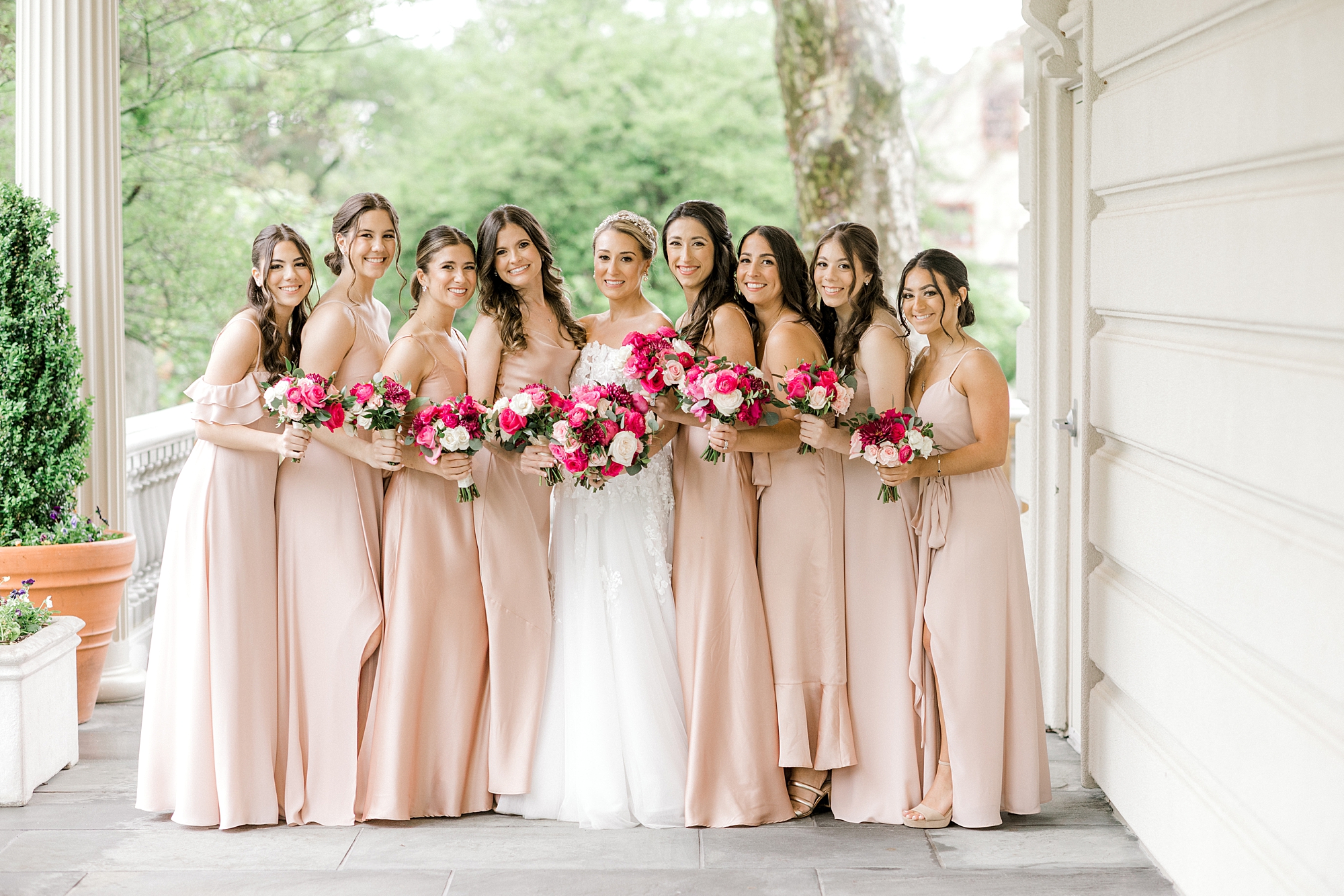 bride poses with bridesmaids in blush gowns holding bright pink flowers