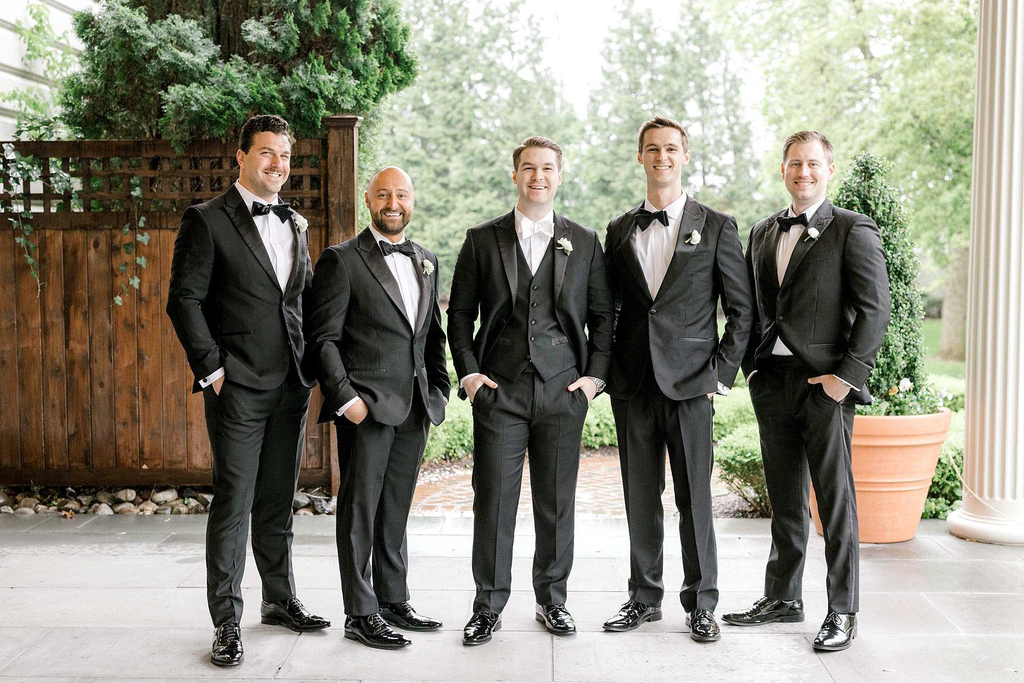 groom stands with groomsmen in black tuxes with hands in their pockets