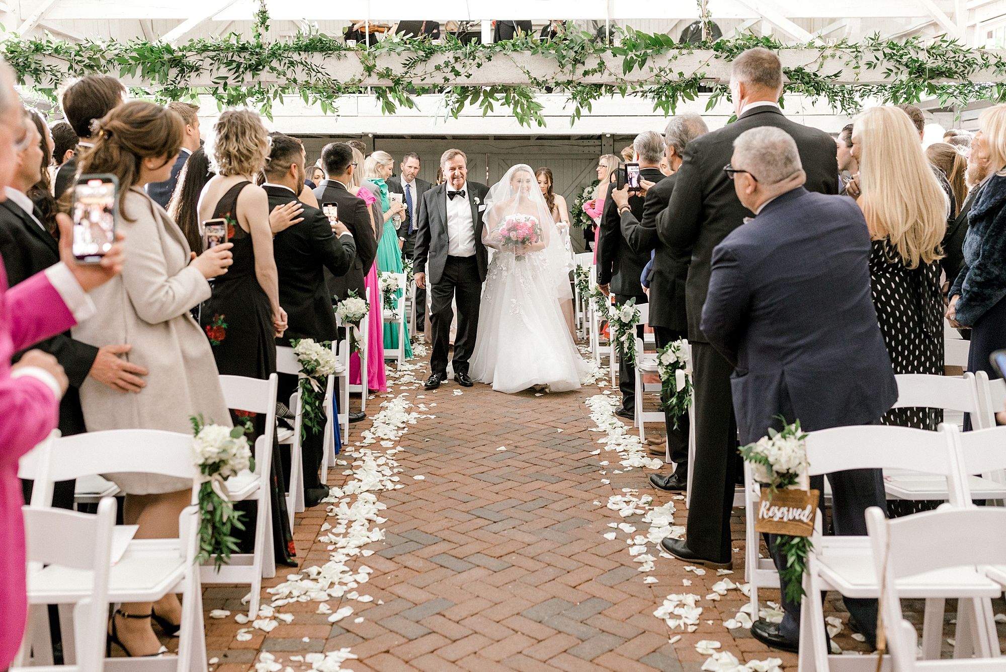 bride walks down aisle with father in barn at The Ashford Estate