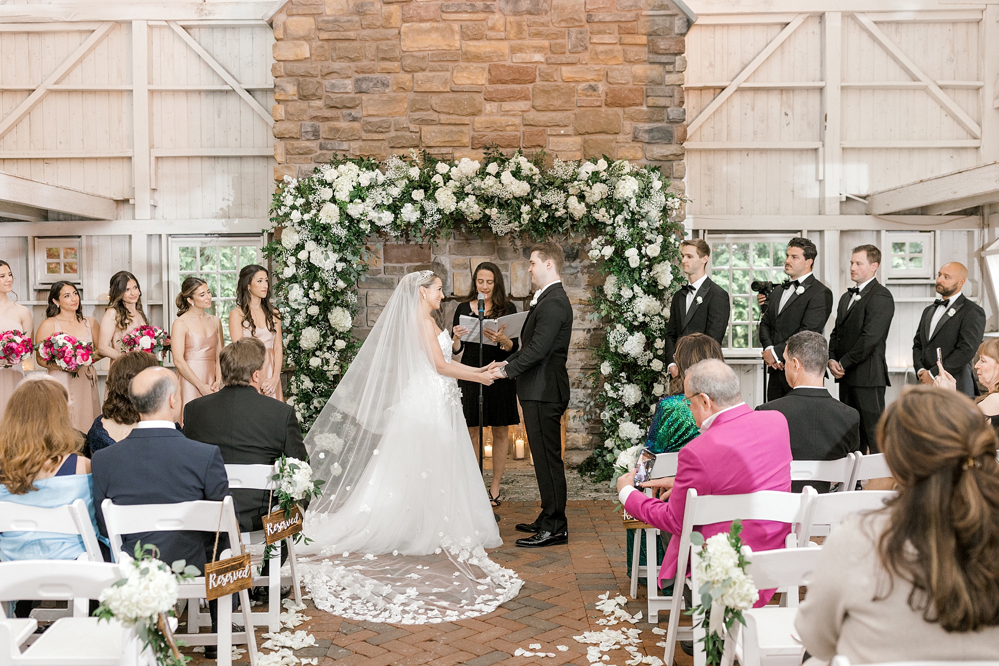 bride and groom hold hands standing in front of stone fireplace with white and green garland at The Ashford Estate