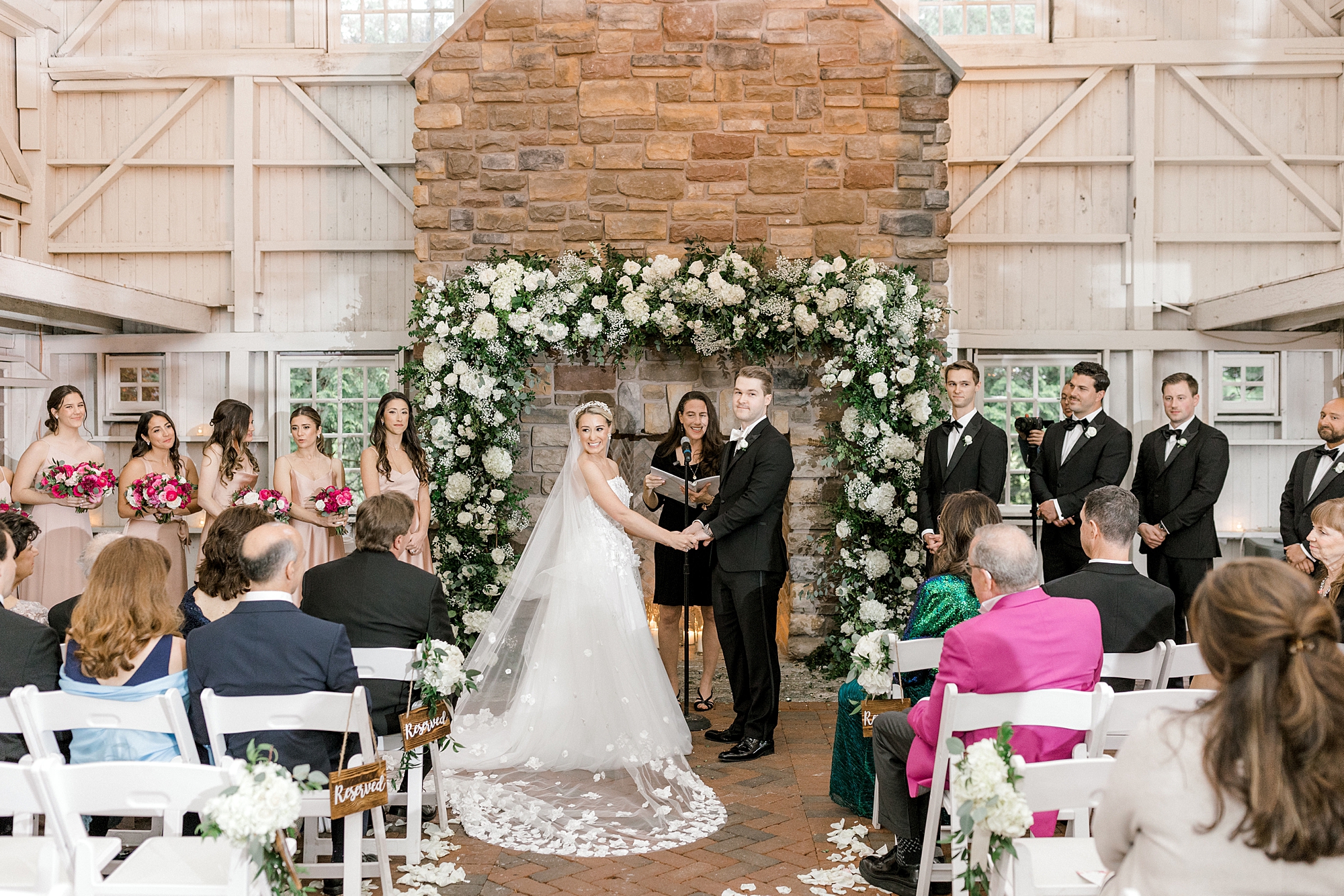 bride and groom hold hands by white flower and greenery garland on fireplace at The Ashford Estate