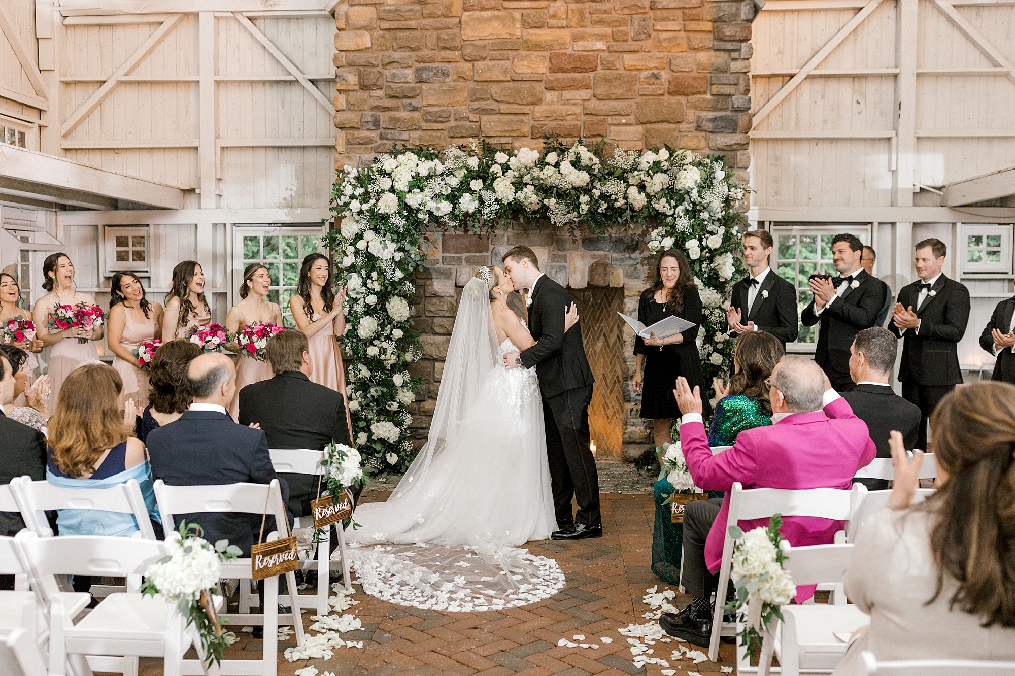 bride and groom kiss in front of fireplace with white flower and greenery garland draped on fireplace