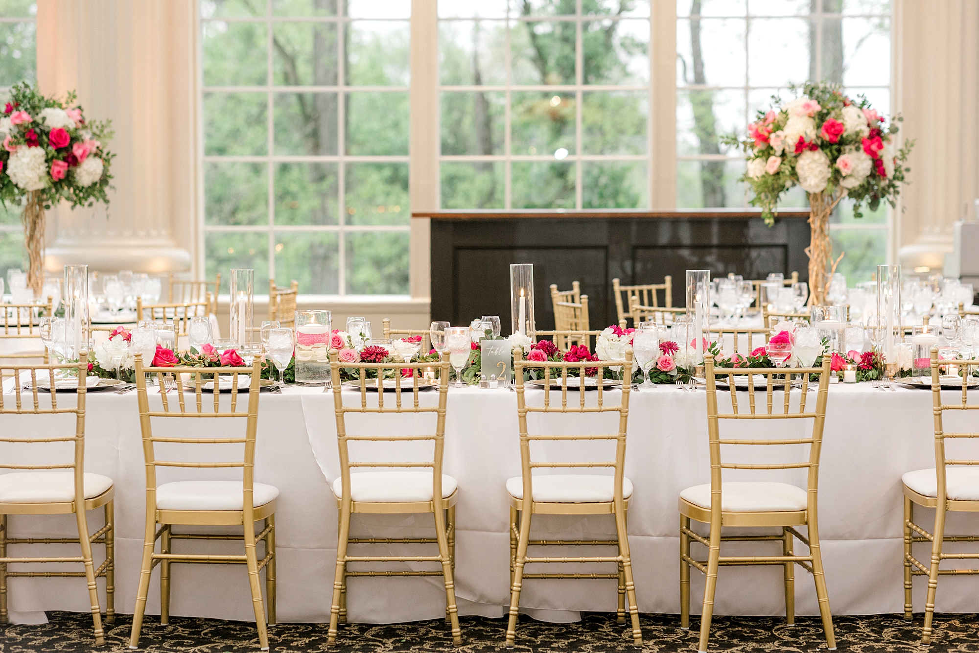 wedding reception table with gold chivalric chairs, pink and white floral centerpieces, and tall white candles