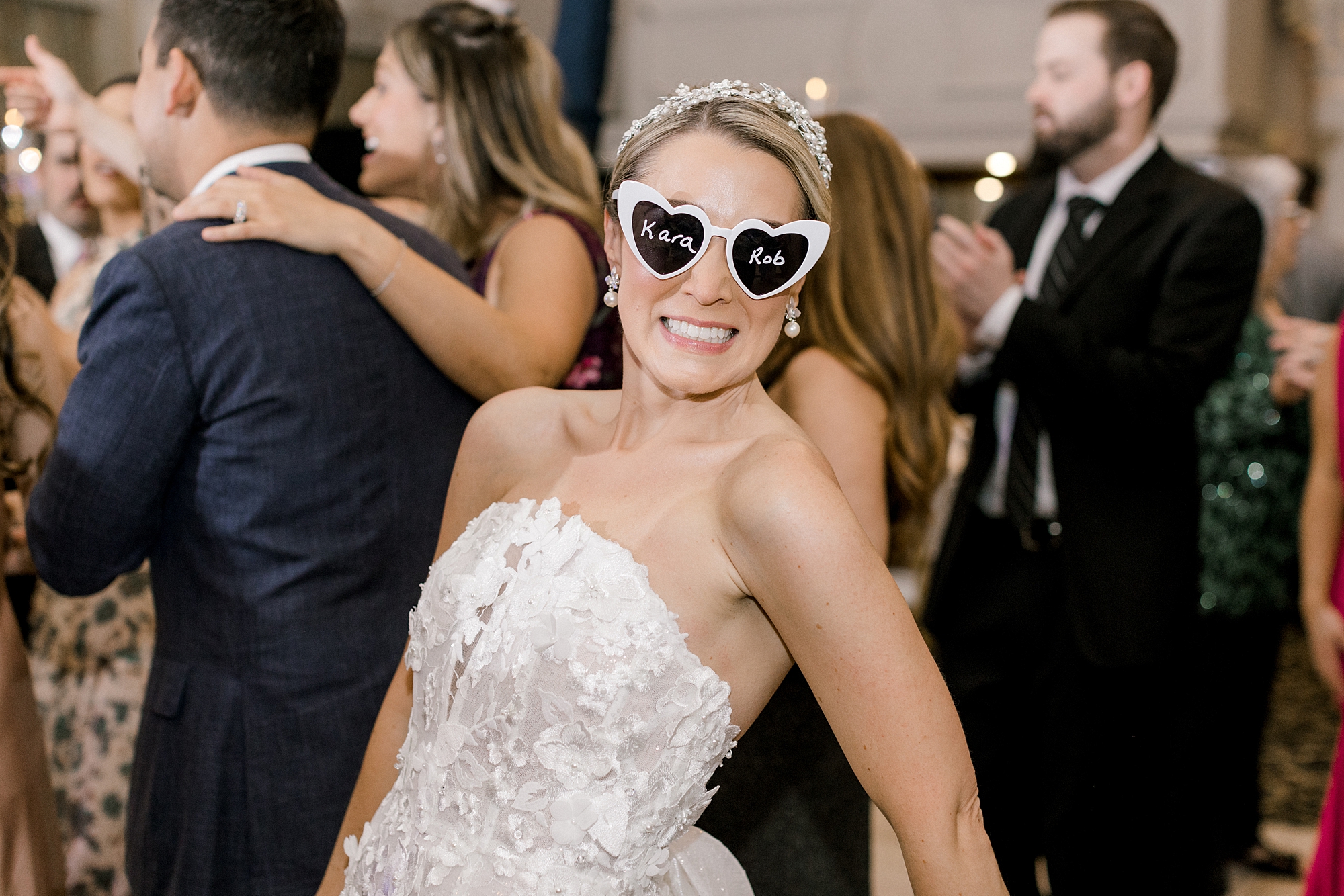 bride in strapless wedding gown smiles wearing heart sunglasses