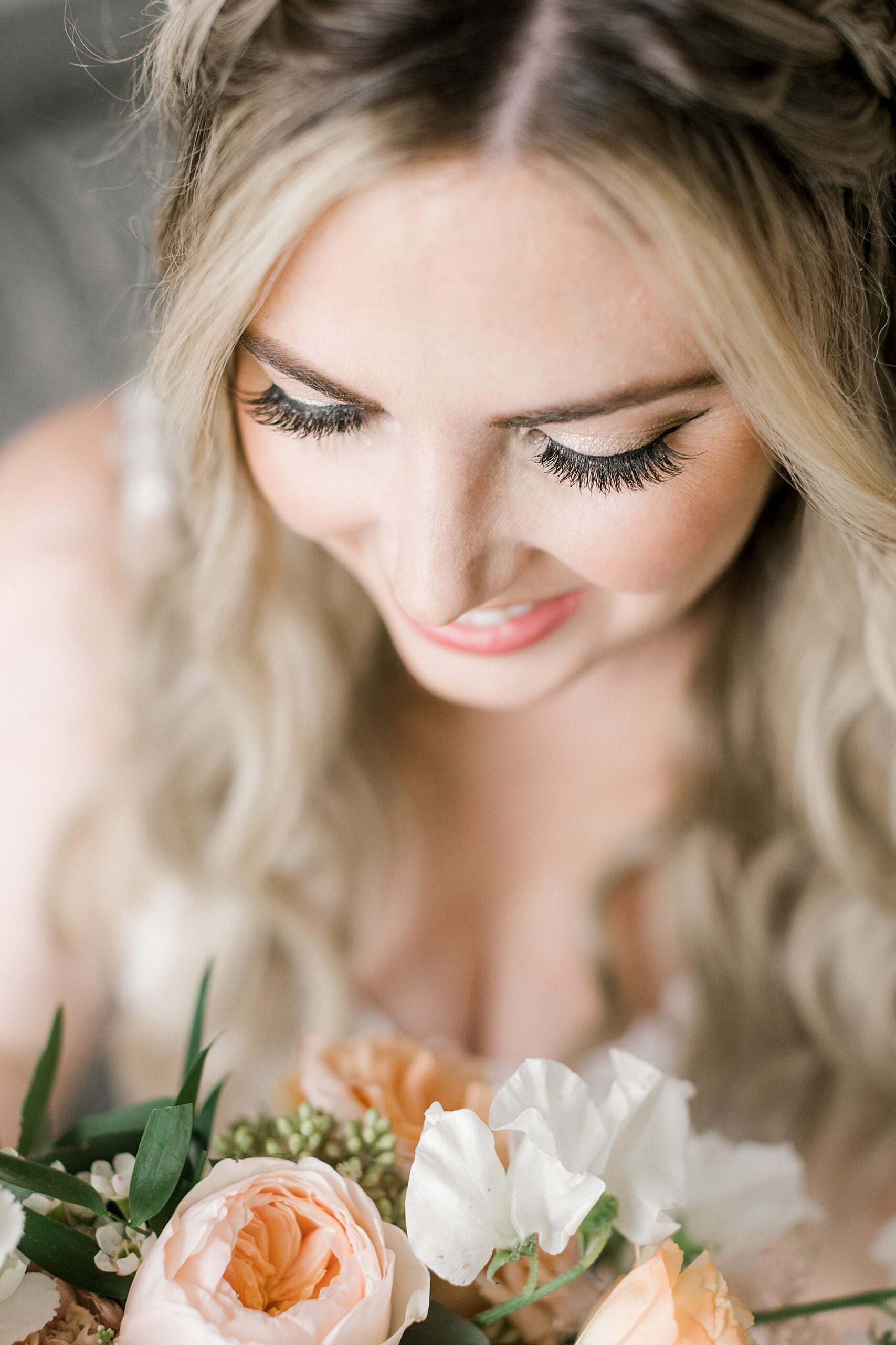blonde bride looks down at peach and ivory bouquet