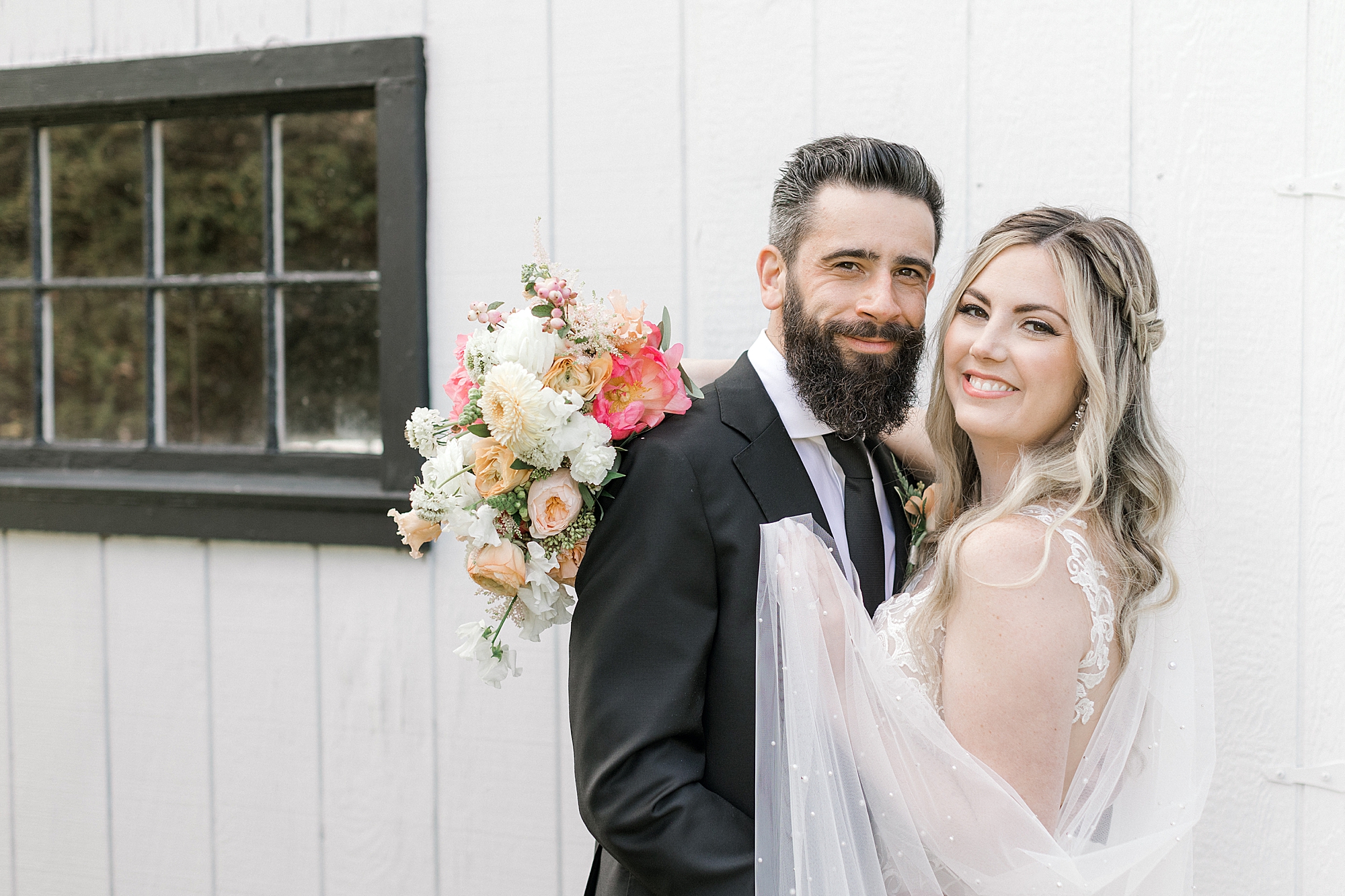 woman hugs man with bouquet around back by white barn at The Townsend Property