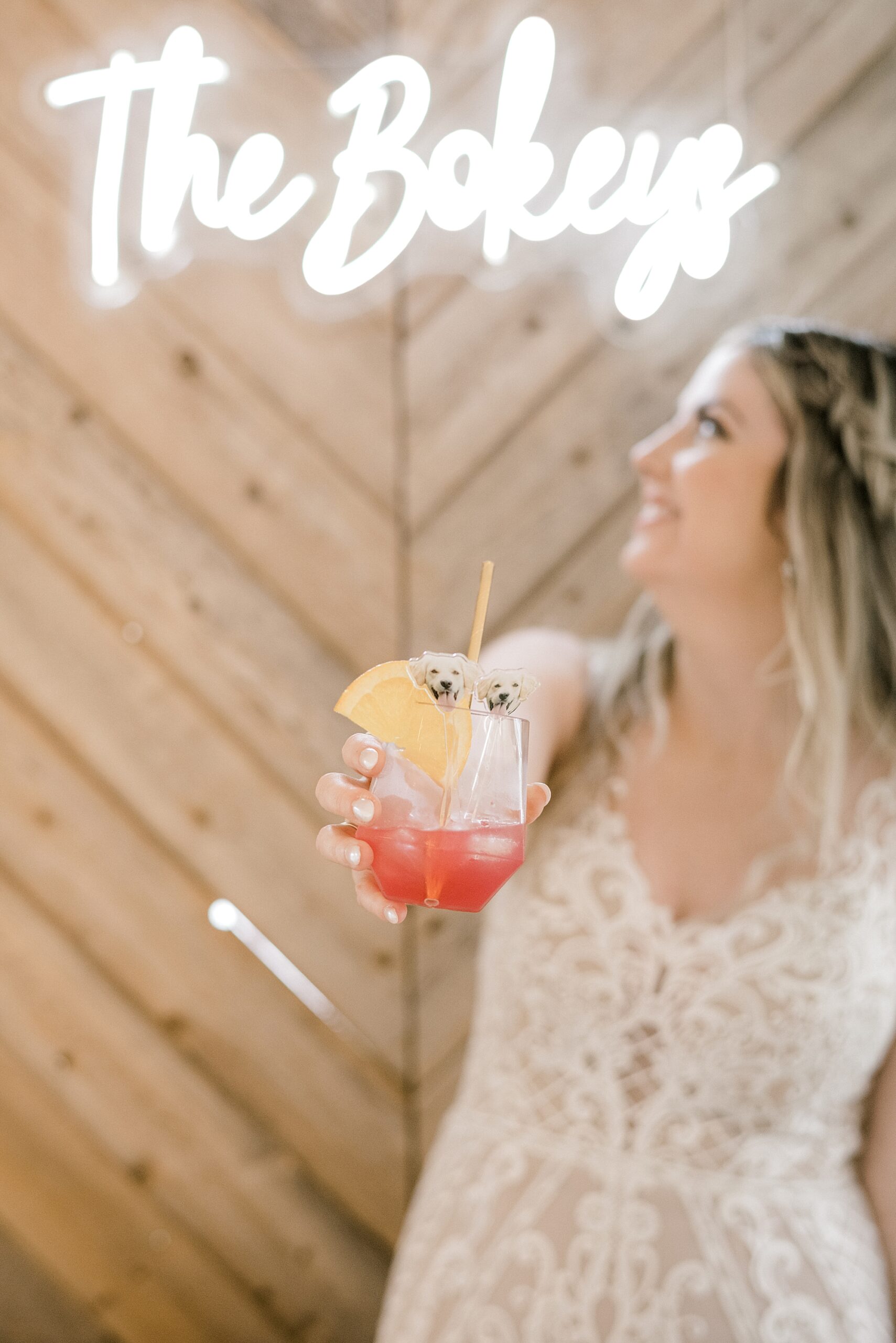 bride holds out cocktail with dog stirrer under neon light