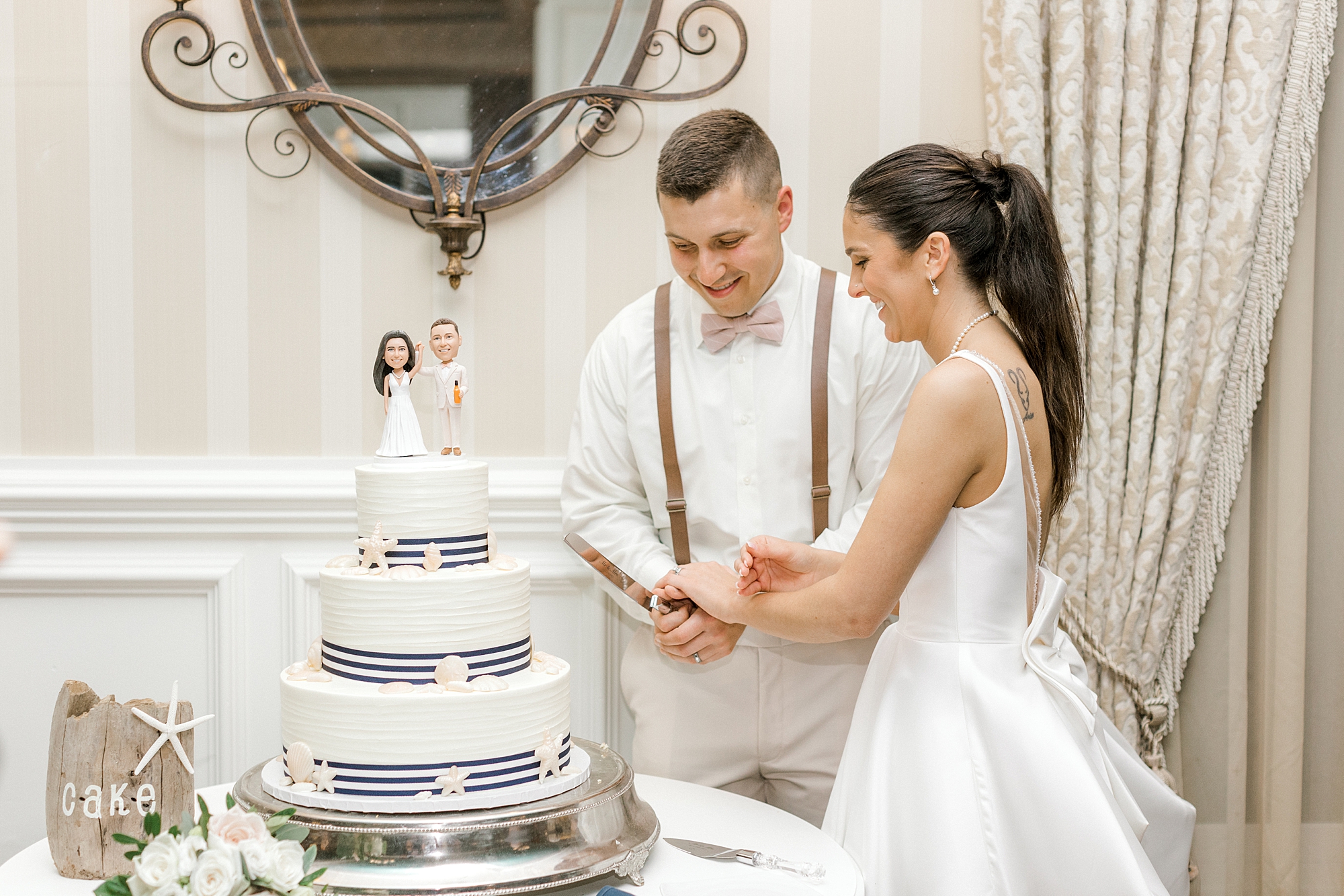bride and groom cut three-tired wedding cake with figurines on top