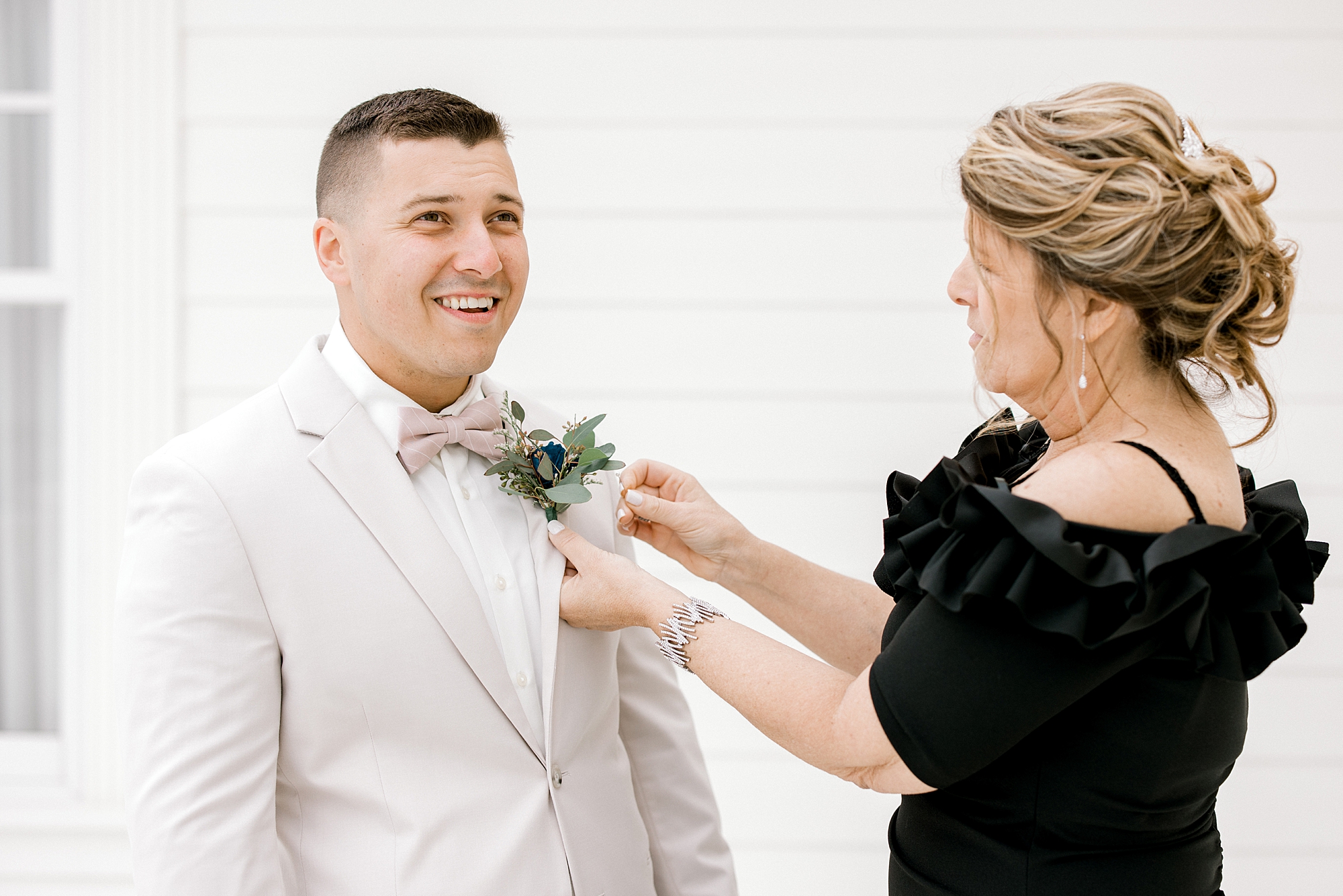 mother adjusts boutonnière for groom on tan suit jacket