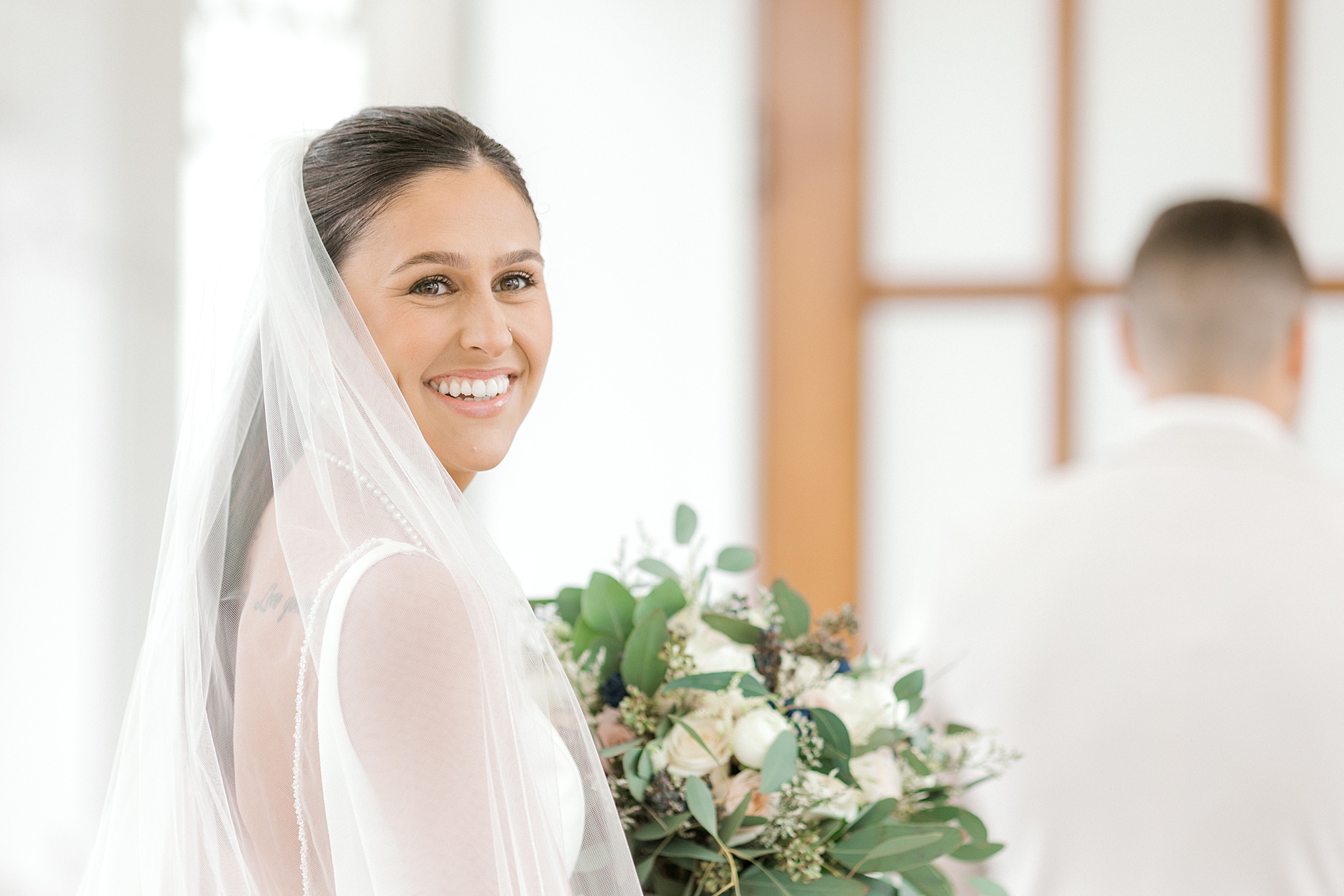 brunette bride looks over shoulder holding bouquet and smiling