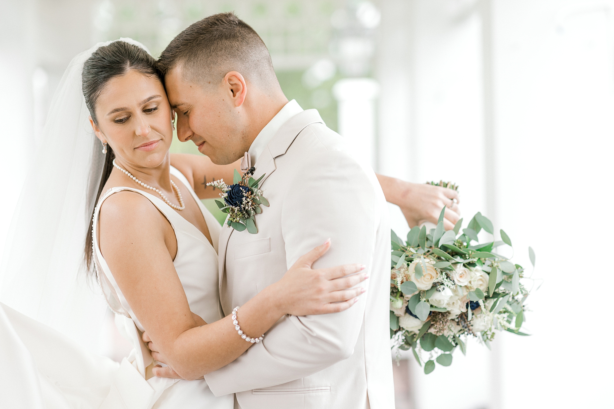 bride and groom hug cheek to cheek with bride's bouquet behind groom's neck
