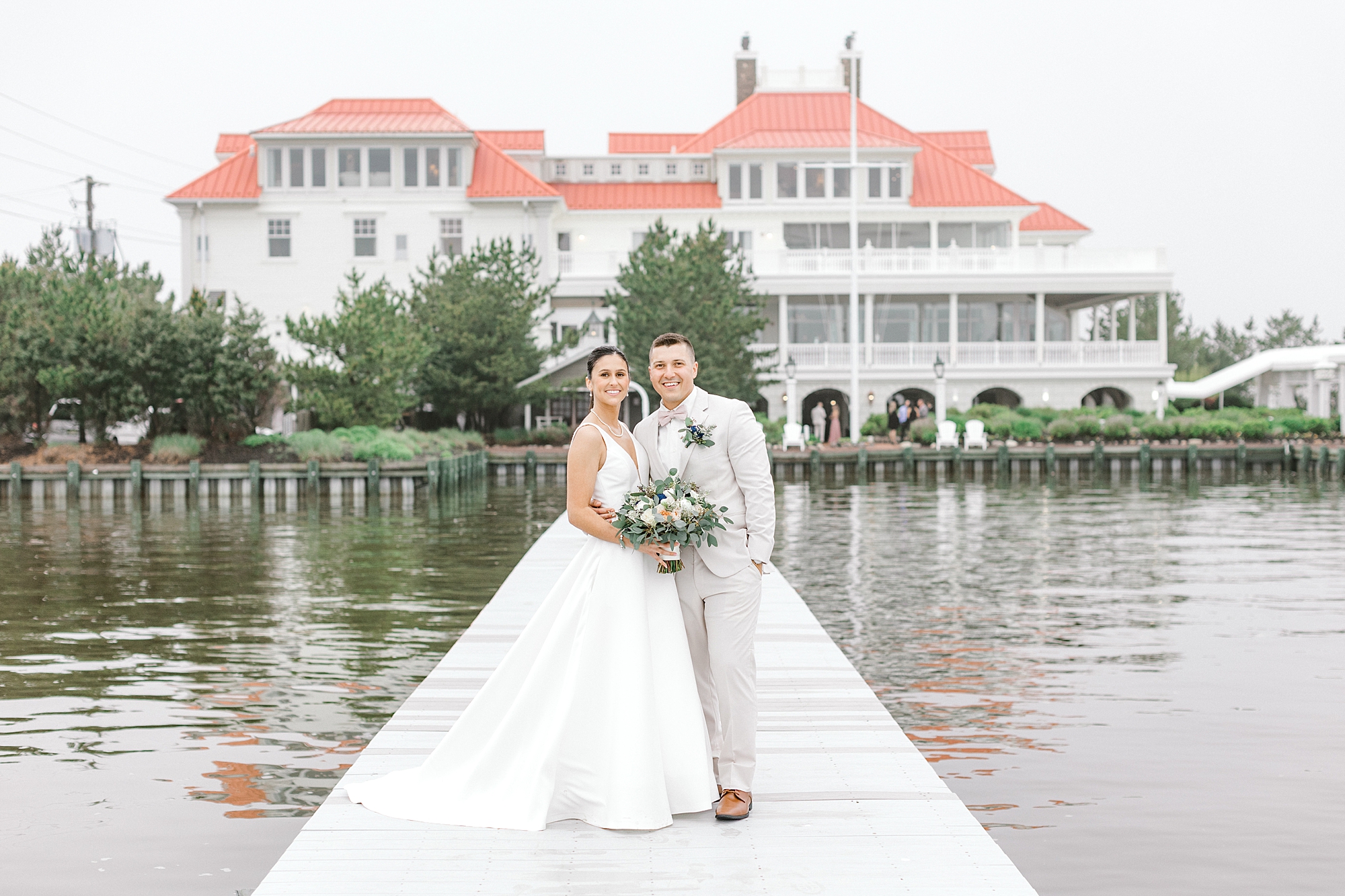bride and groom hug on dock in front of Mallard Island Yacht Club