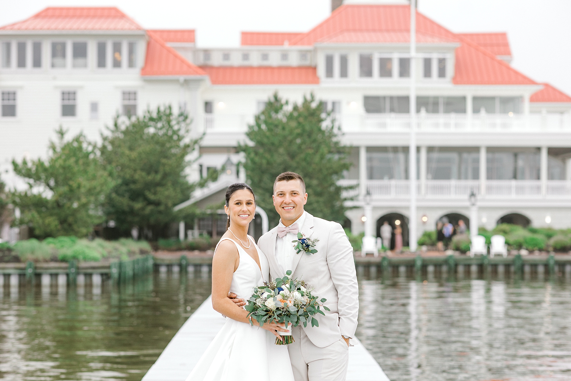 newlyweds stand on dock in front of Mallard Island Yacht Club