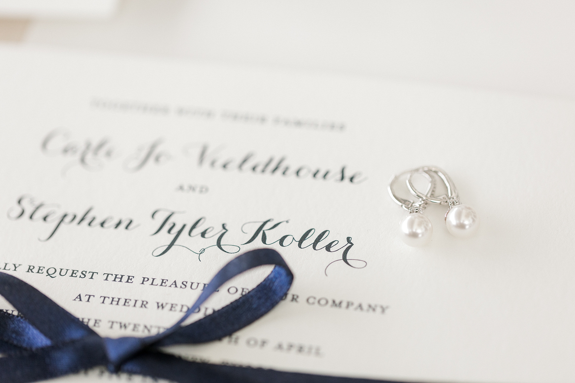 stationery with blue calligraphy, blue ribbon and diamond earrings resting on top